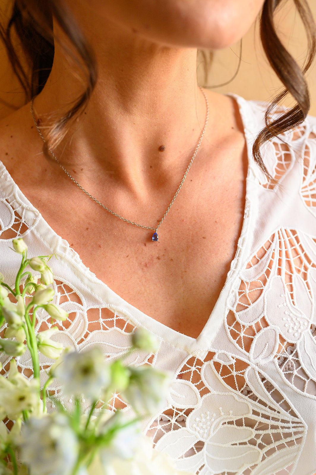 femme portant un collier avec une pierre bleu en robe de mariée et avec des fleurs