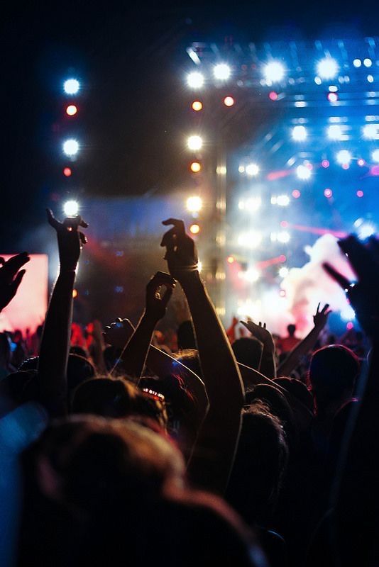 Beaucoup de monde les mains en l'air avec en fond des projecteurs montrant qu'ils sont dans un festival de musique