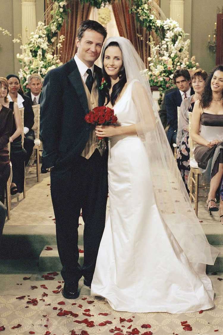 Chandler et Monica souriant à l'objectif dans leur tenues de mariage et accessoires de mariés