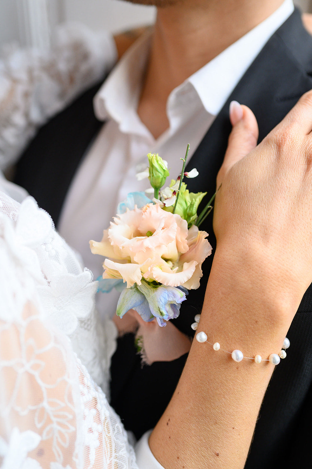 fleur accrochées au costume d'un marié avec sa femme qui mets sa main sur son épaule portant un bracelet en perle naturelle