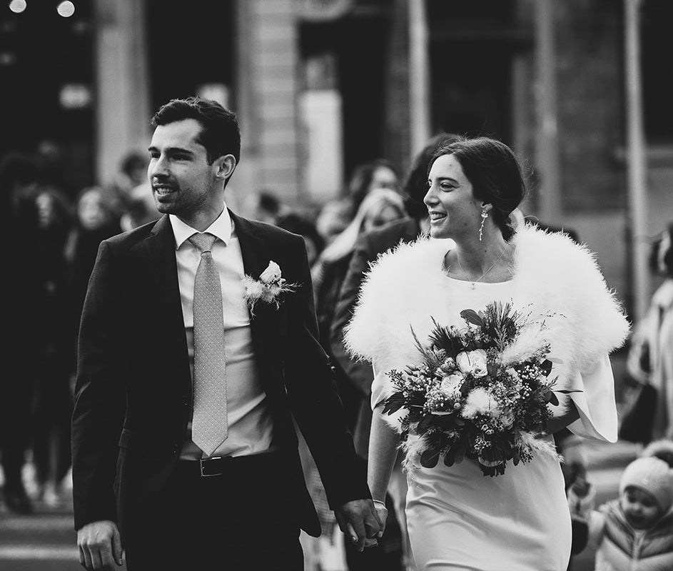 Jeunes mariés se tenant la main en marchant, vêtus de leurs tenues de mariage et accessoires