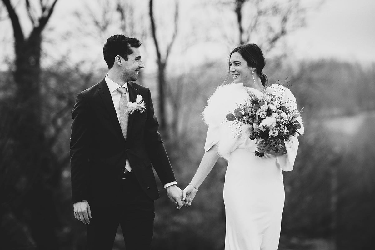 Jeune couple se tenant la main en souriant avec des tenues et bijoux de mariage d'hiver 