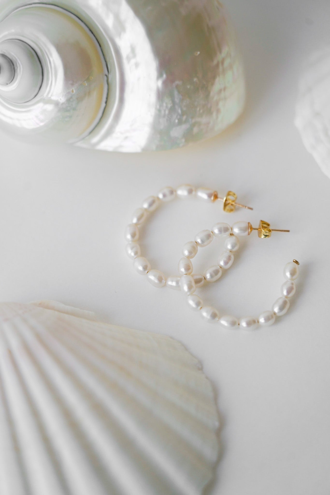 boucles d'oreilles en perles naturelles en forme de créoles sur une table avec deux coquillages 