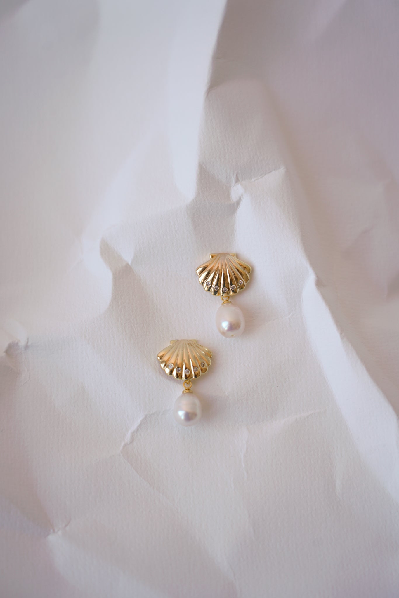 boucles d'oreilles mariage en coquillage sur une feuille blanche froissée