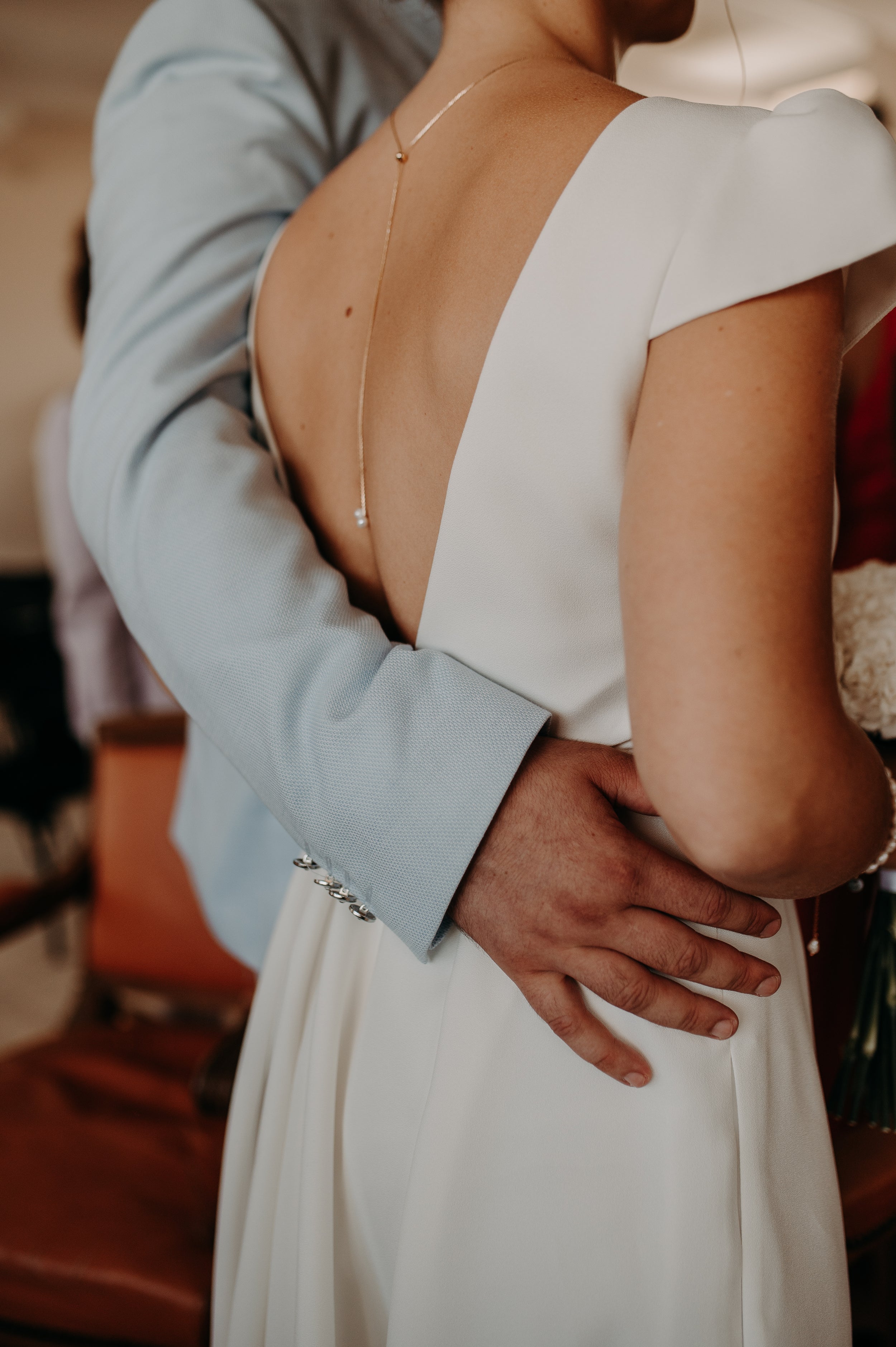 Femme de dos avec la main de son mari sur sa taille montrant sa robe avec son décolleté de dos et son collier de dos en perles naturelles