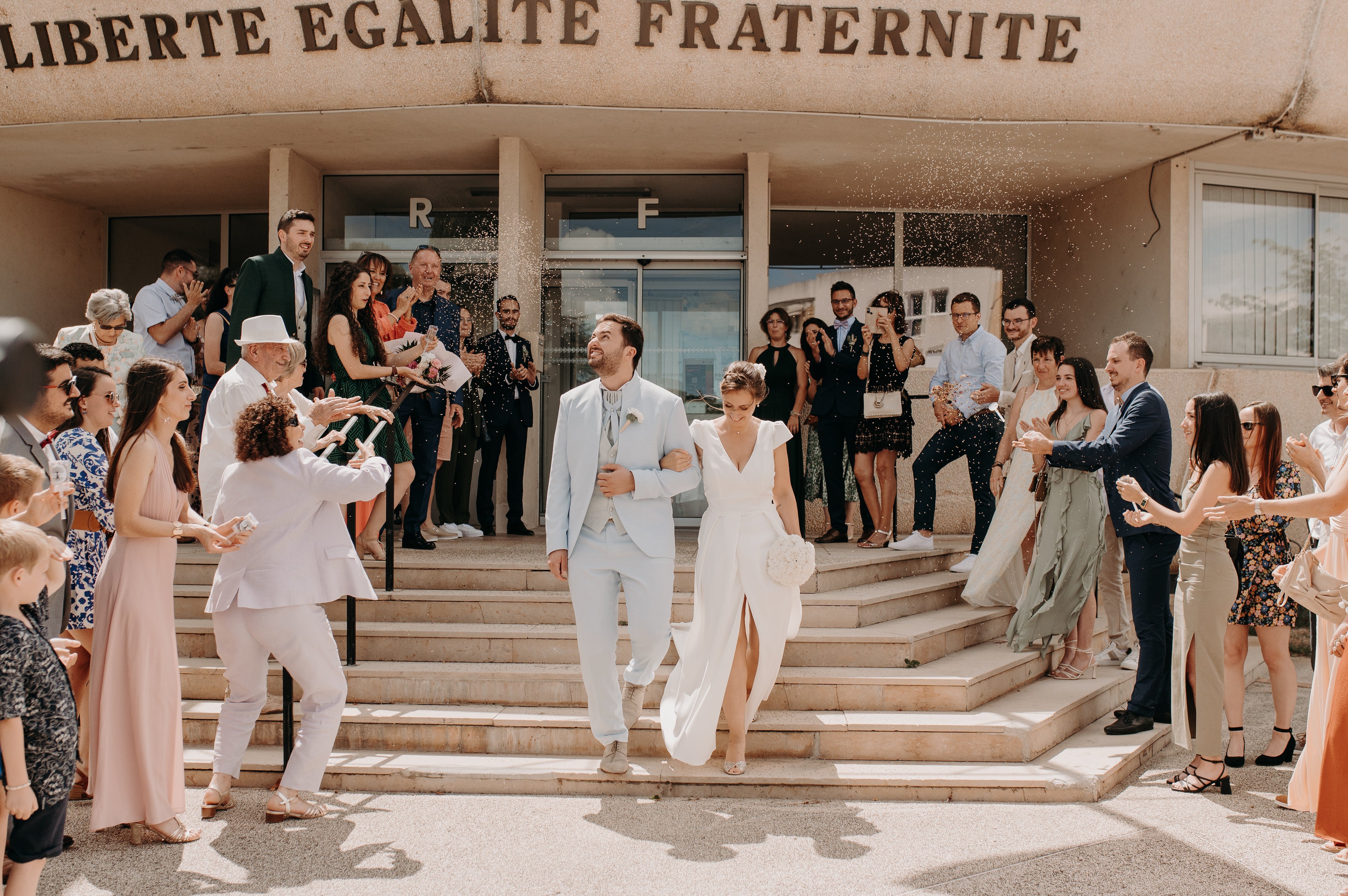 Les deux jeunes mariés se tenant par le bras souriant en sortant de la mairie