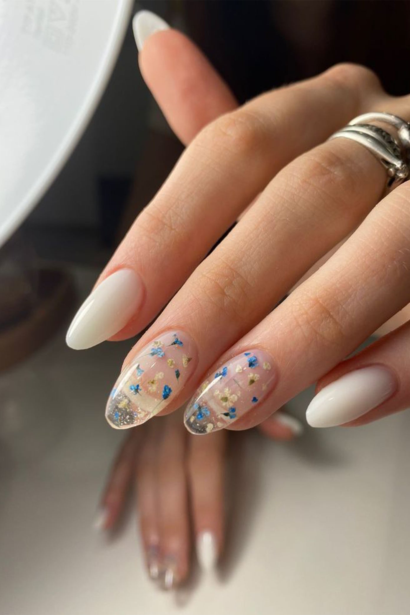 Ongle long pour future mariée avec des ongles transparents comportant des fleurs bleues incrustées ainsi que des ongles mate