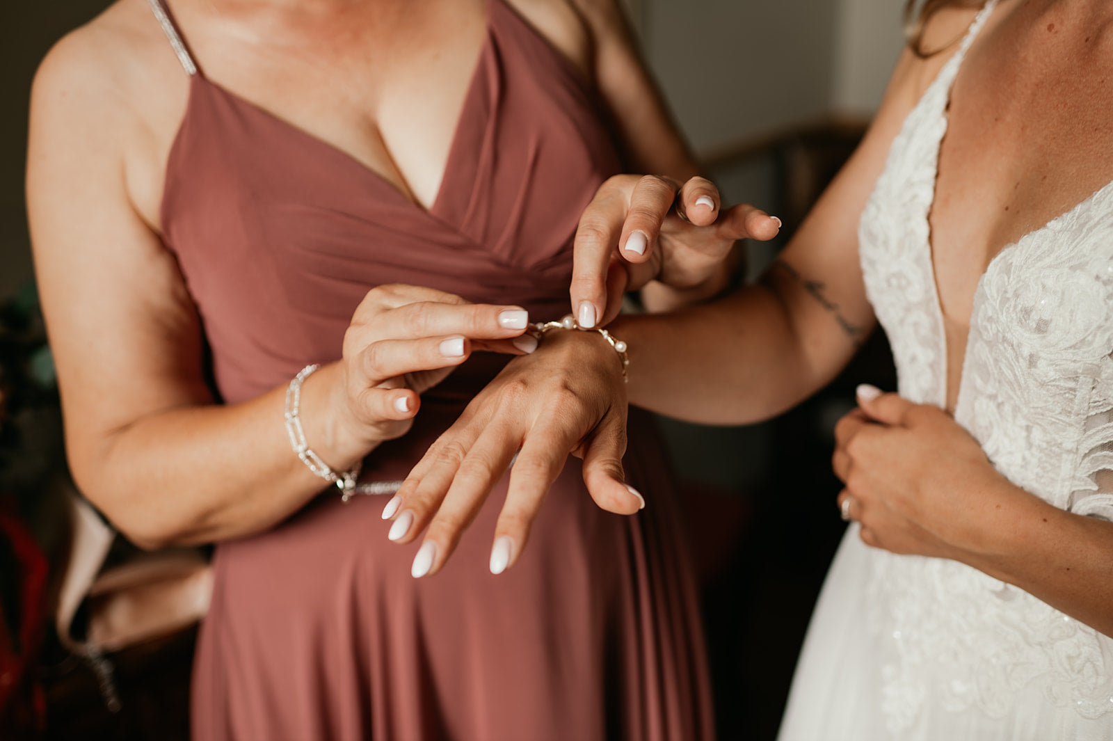 Focus sur la demoiselle d'honneur qui met le bracelet de la mariée en robe blanche