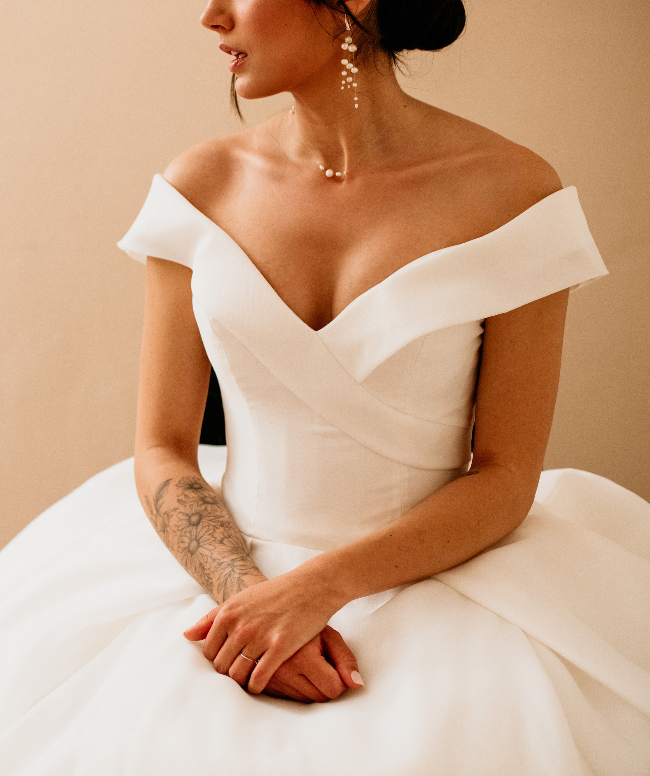 Focus sur le buste de la mariée montrant sa robe en col bardot et ces bijoux notamment son collier et ces boucles en perles naturelles