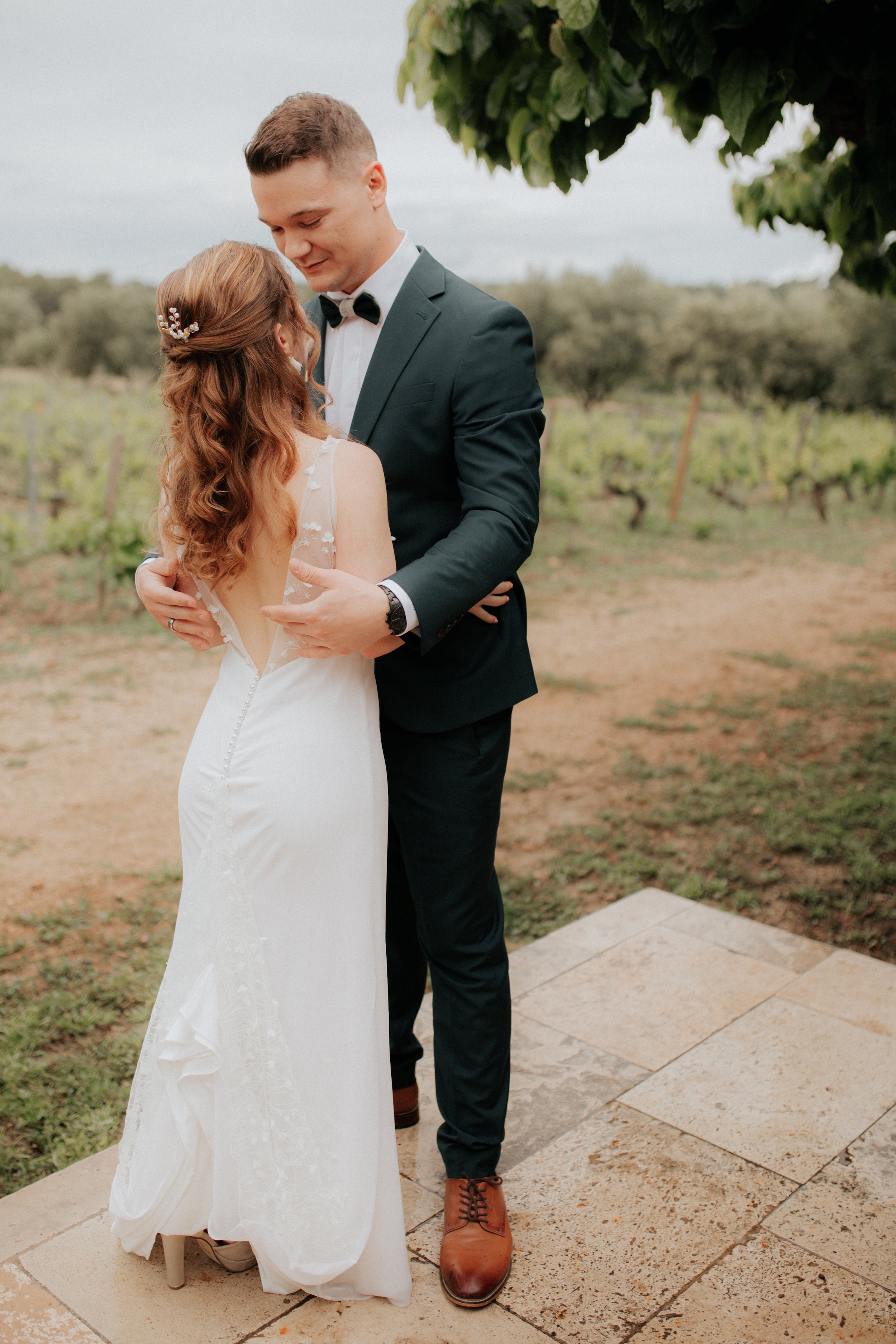 Les mariés qui s'enlacent dans leurs tenues de mariage avec la mariée de dos montrant son accessoires pour les cheveux