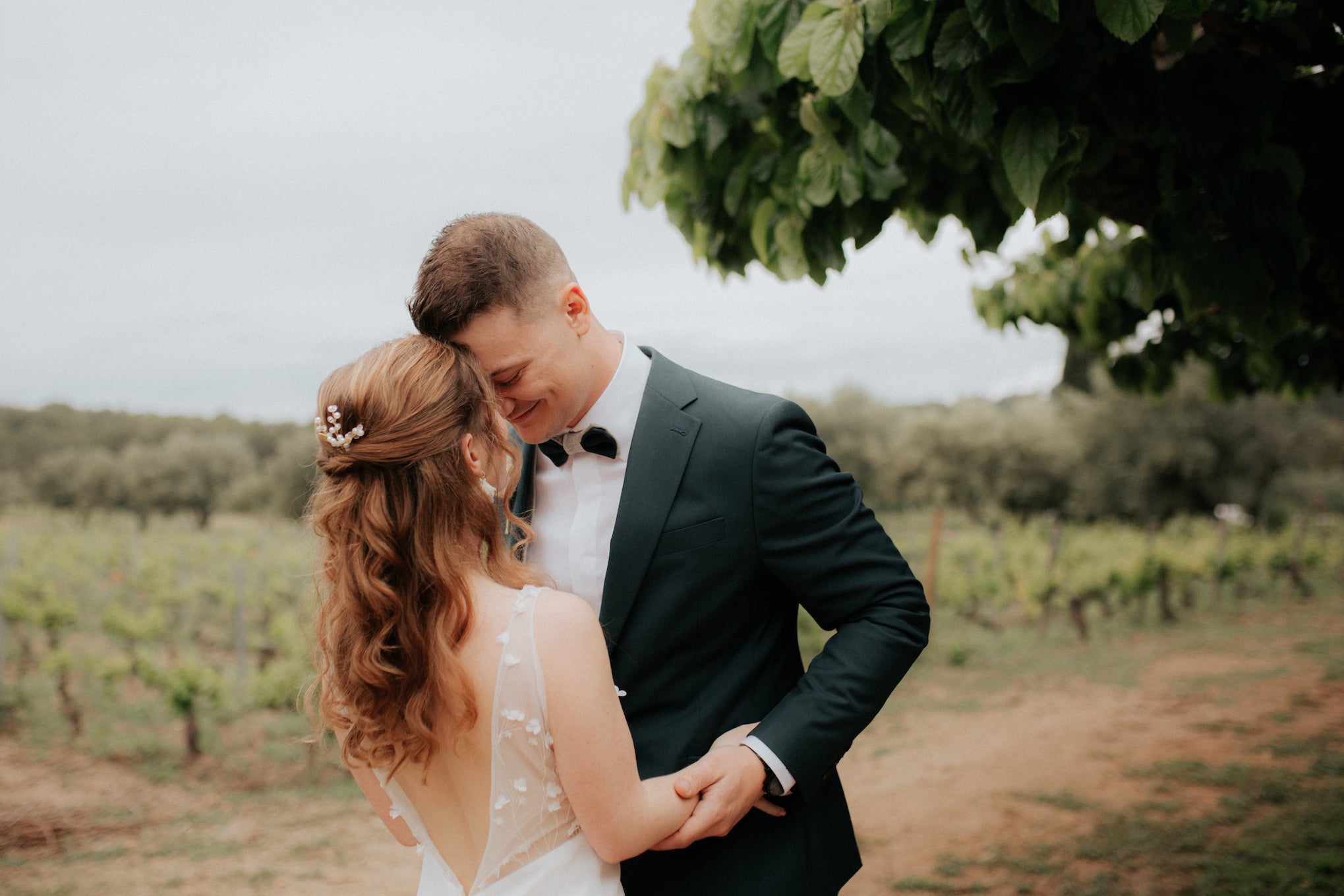 Mariés front contre front avec la mariée de dos montrant sa coiffure de mariage avec une pic florale