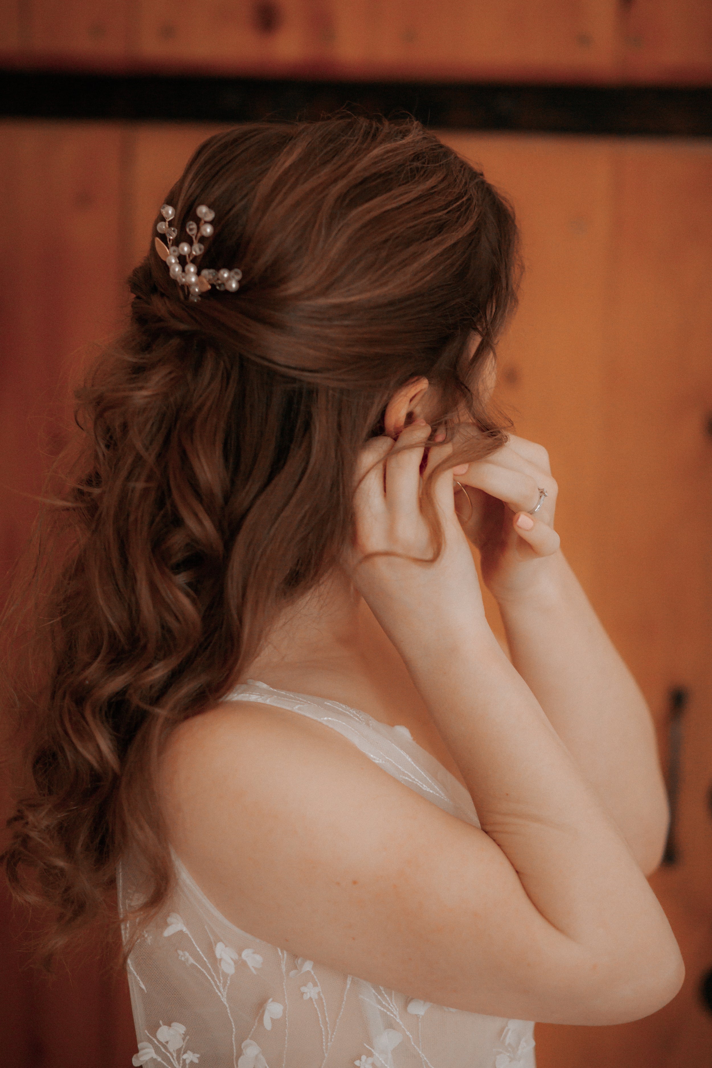 Mariée qui se prépare en mettant ses boucles d'oreilles de mariage et en montrant sa pic à cheveux en perles naturelles