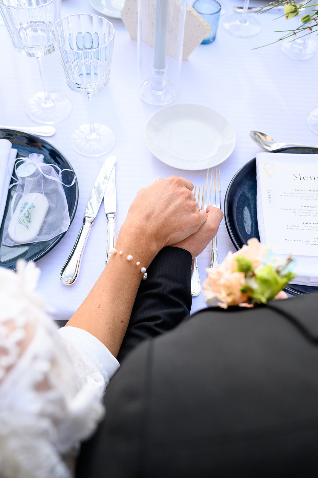 couple se tenant la main sur la table d'honneur le jour de leur mariage et portant un bracelet de mariée en perles naturelles 