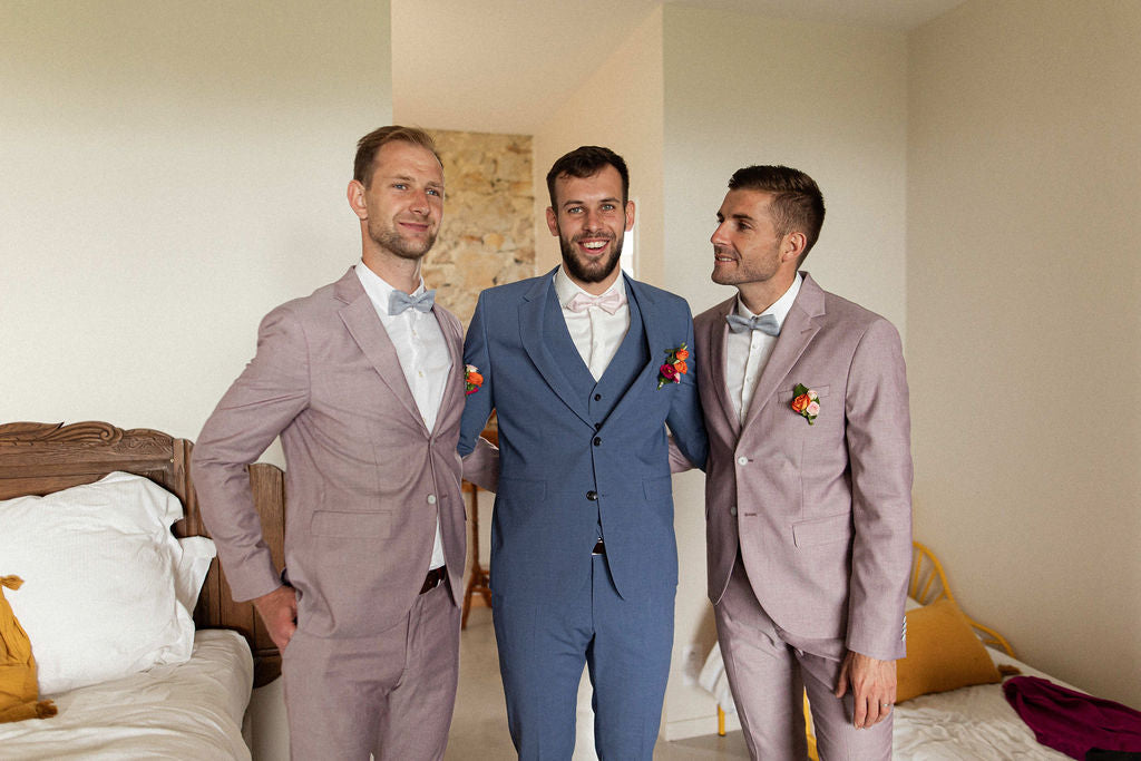 la mariée et ses témoins pour le jour du mariage habillés en costume lilas et bleu marine souriant entre eux