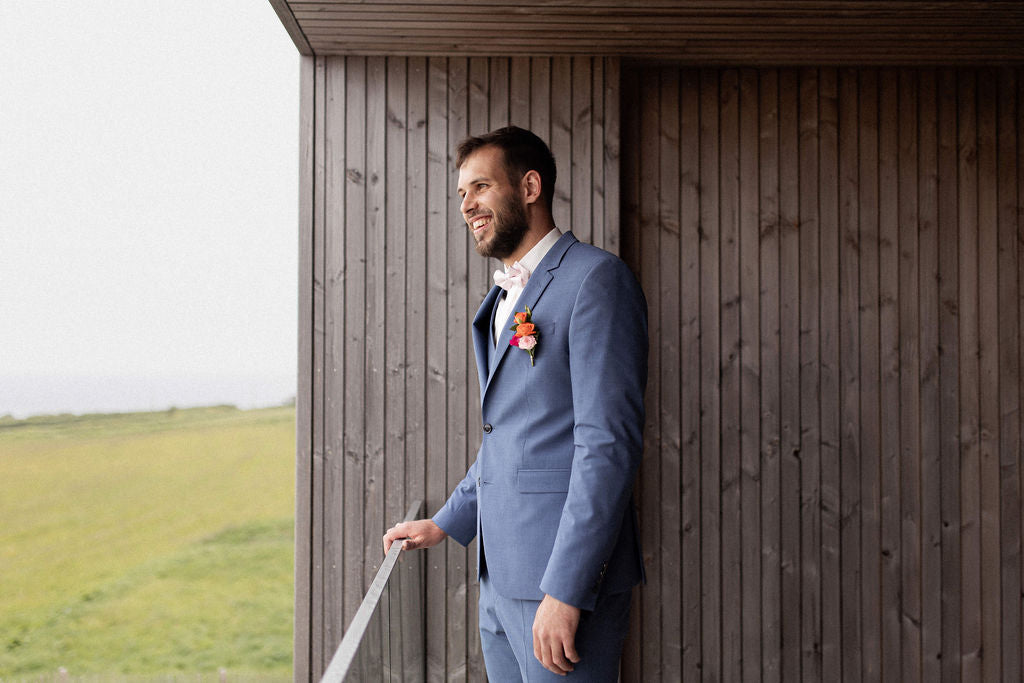 homme souriant portant un costume bleu marine et une chemise blanche sur une terrasse en bois