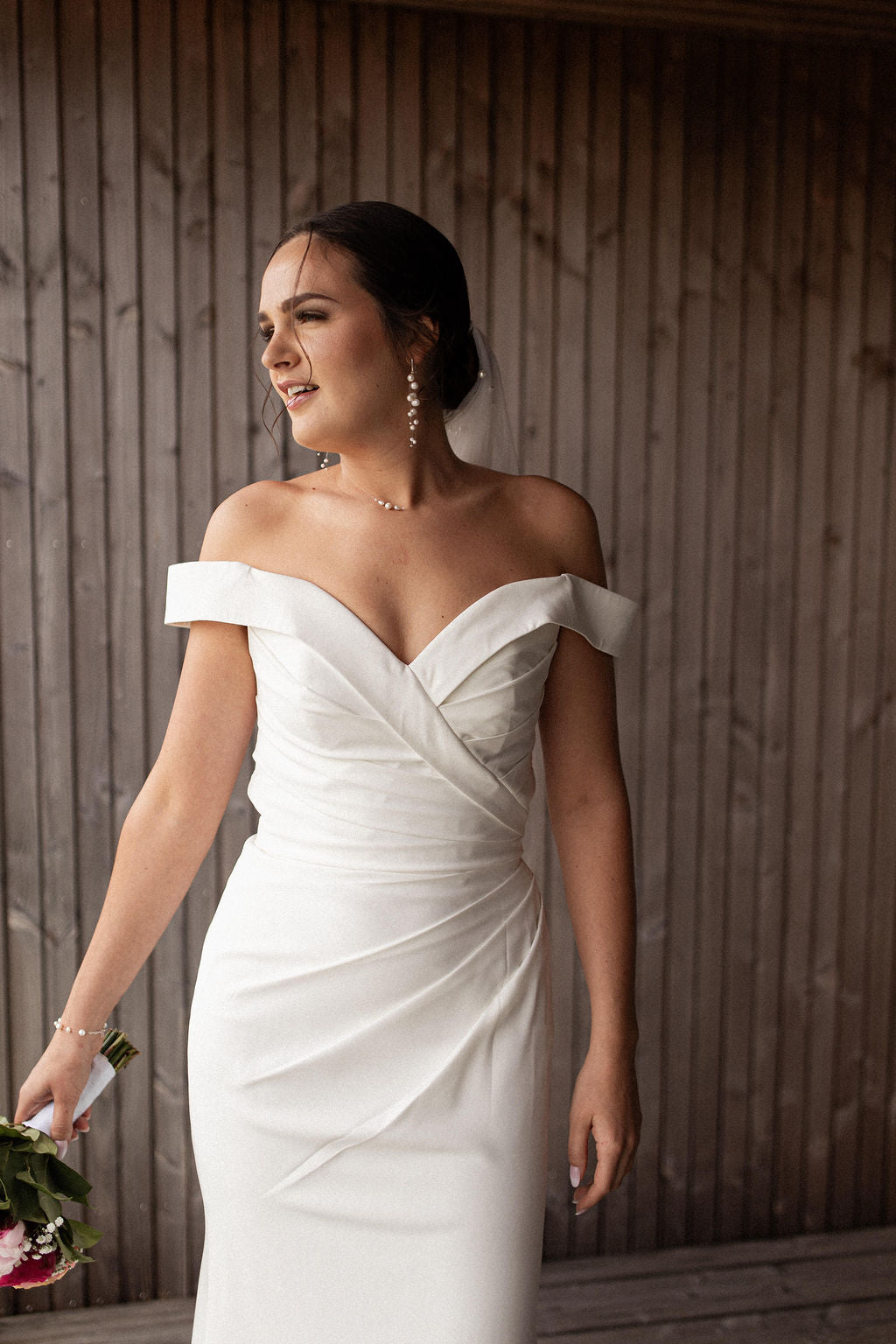 femme en tenue de mariée portant une robe blanche bustier col bateau portant un collier et des boucles d'oreilles en perles naturelles