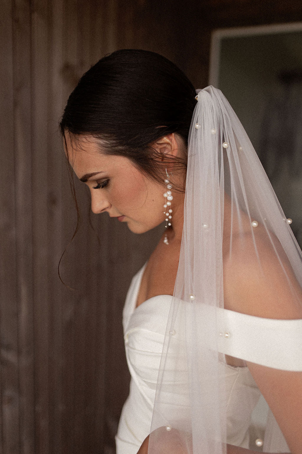 femme penchant la tête vers l'avant en robe de mariée avec un voile et des boucles d'oreilles en perles naturelles