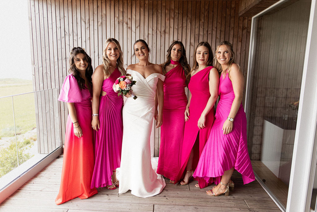 six femmes souriantes dont cinq demoiselles d'honneurs habillées en rose et la mariée en blanc pour le jour du mariage 