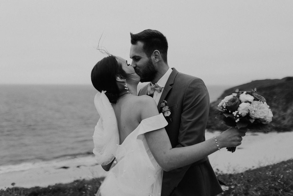 deux mariés sur le bord de la plage la mariée tient son bouquet dans les mains et le mari l'embrasse