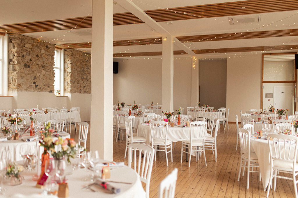 salle remplie de tables et de chaises blanches pour un mariage, parquet au sol et décoration de table colorée et florale