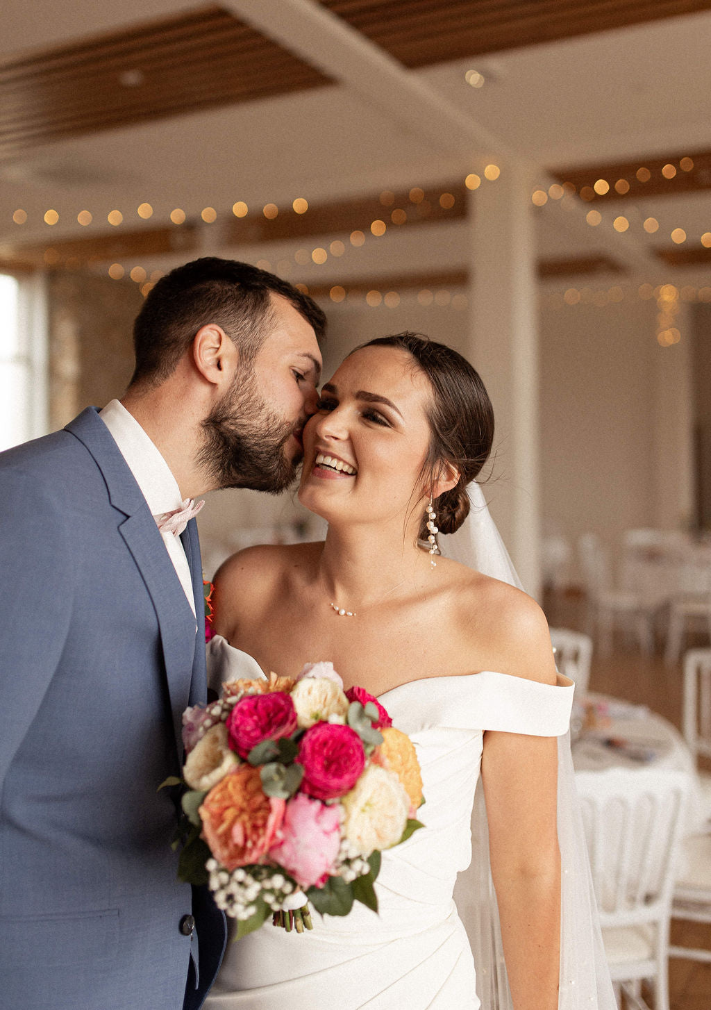 couple de mariés le jour du mariage la femme tient un bouquet de fleurs et des bijoux en perles naturelleset l'homme lui fais un bisou sur la joue