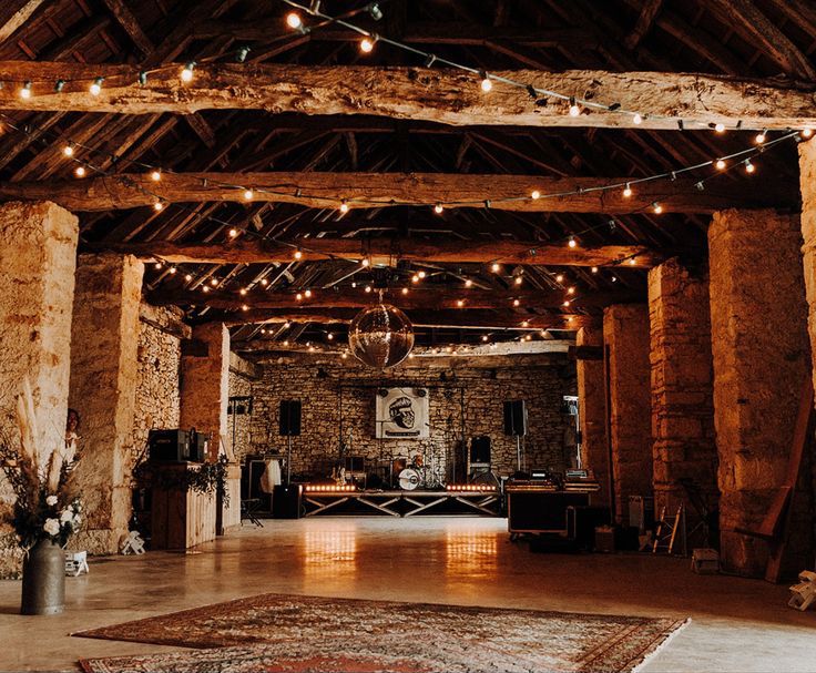 salle de mariage boheme avec des poutres au plafond et du carrelage beige avec une scène pour acceuillir un groupe de musiaue