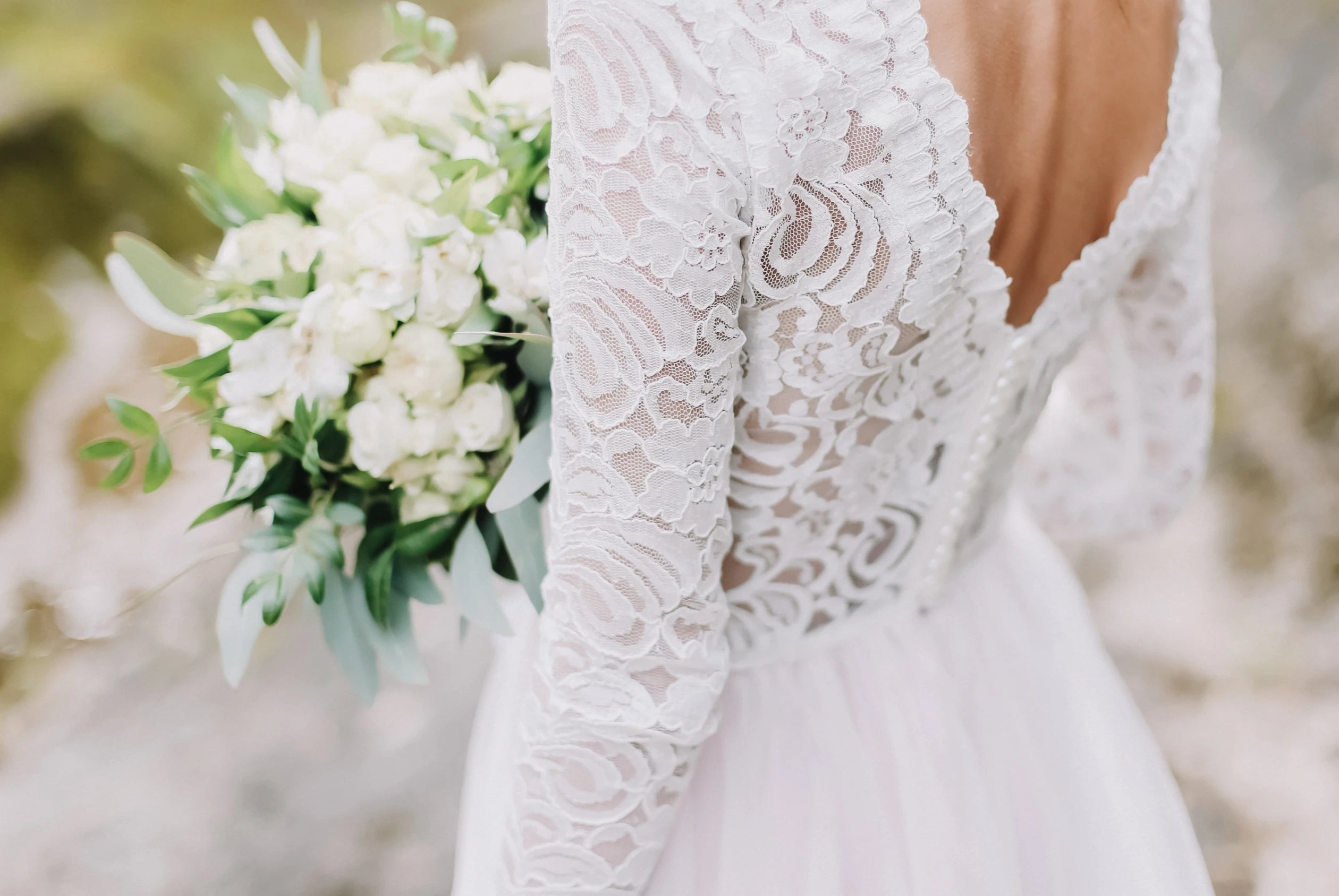 Mariée de dos montrant sa robe de mariage à manches longues en dentelle avec un décolleté de dos plongeant