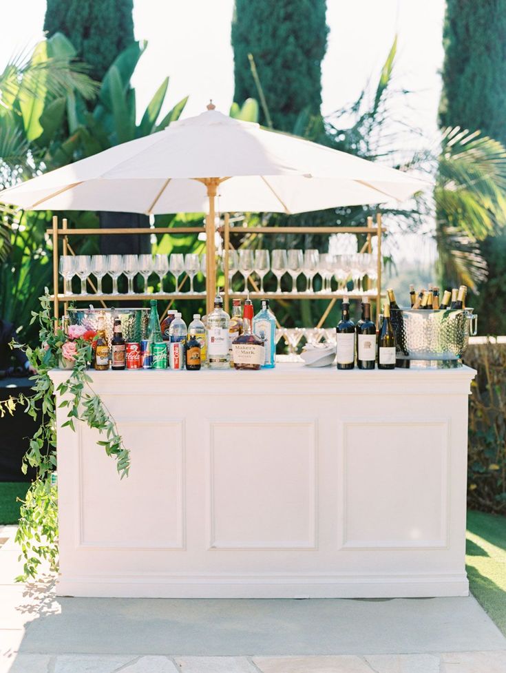 bar à cocktails blanc avec parasol blanc et des bouteilles de couleurs pour une animation de mariage 