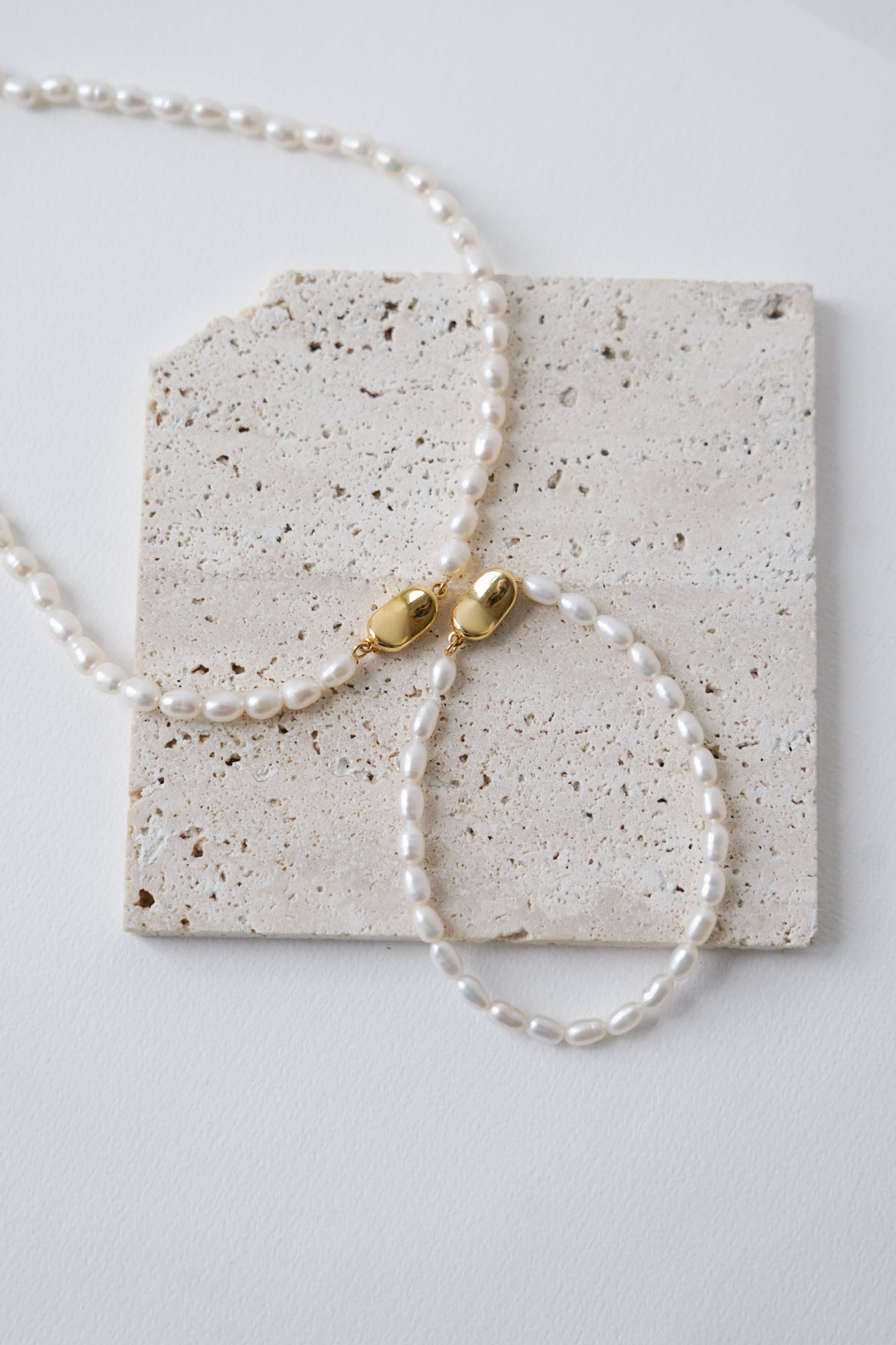 un collier et un bracelet de mariage en perles naturelles avec un fermoir doré sur une pierre naturelle beige