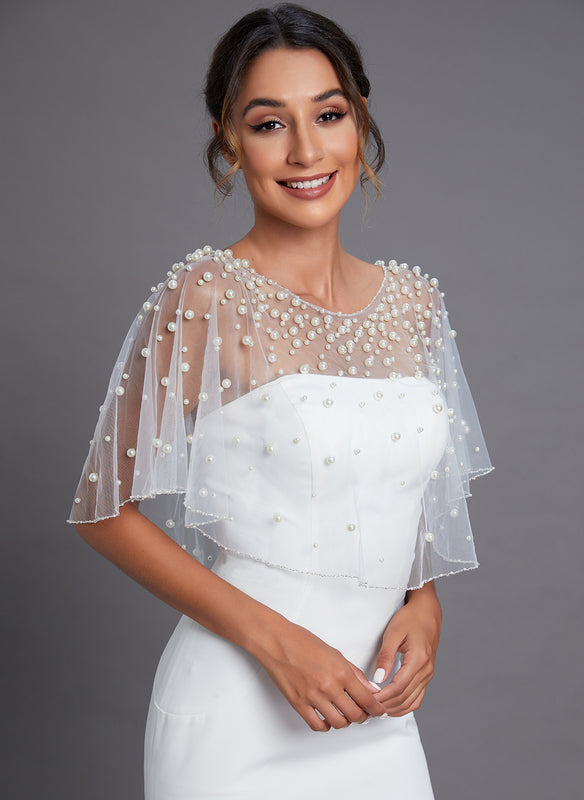 Mariée qui souri en portant sa tenue de mariage notamment une cape brodée avec des perles naturelles