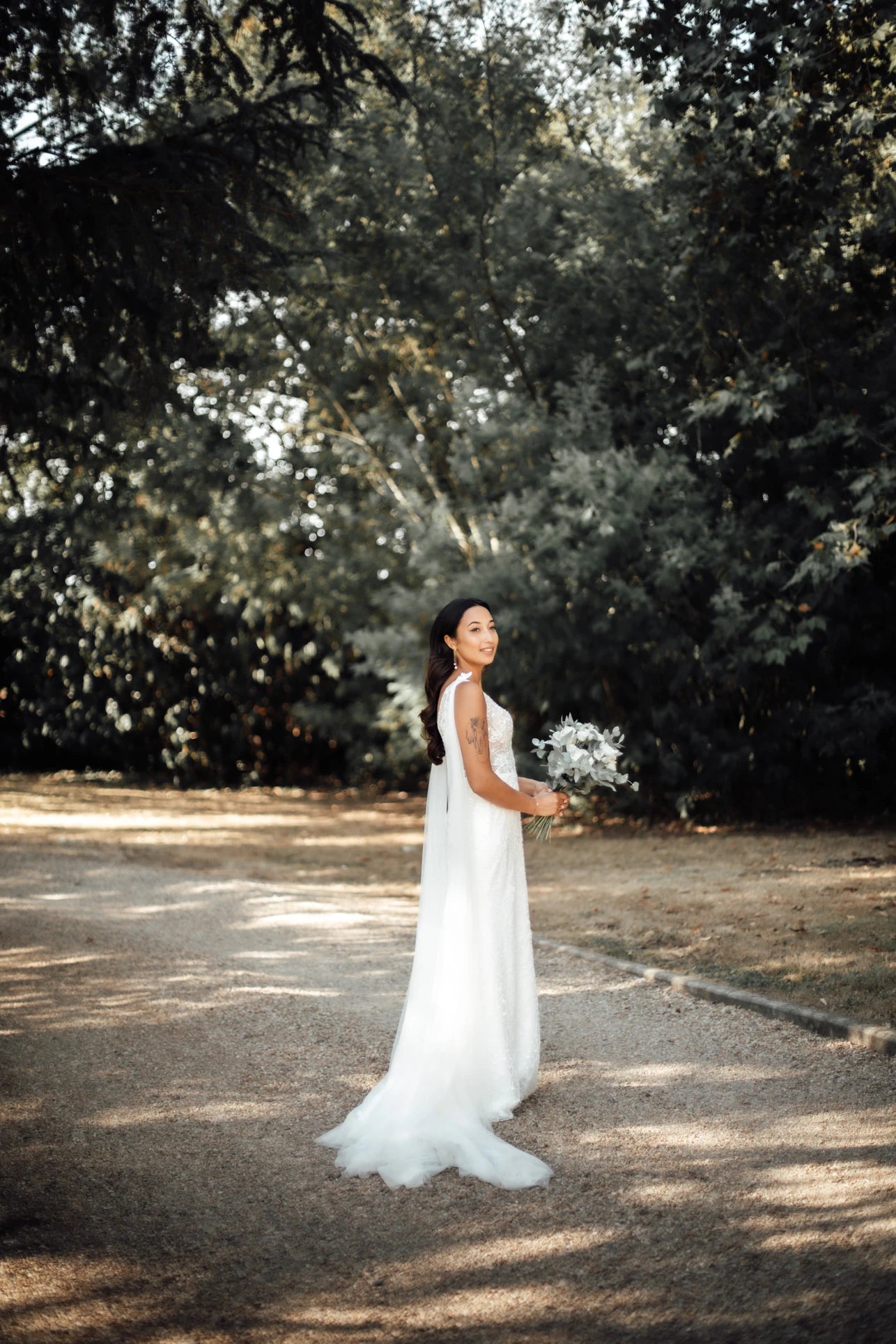 Jeune femme en tenue de mariage de profil dehors tenant son bouquet et portant ses bijoux