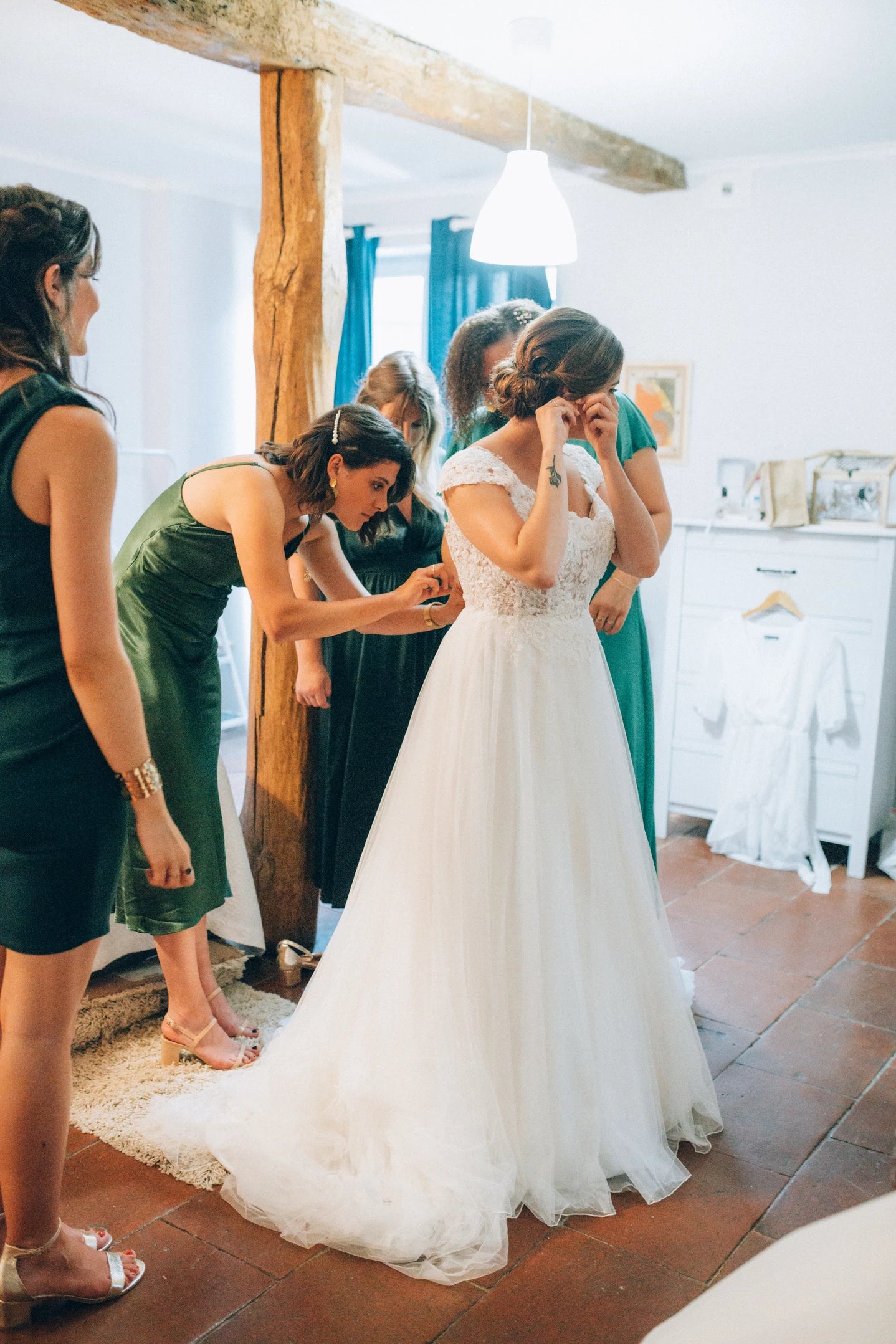 Mariée qui se prépare en mettant ses boucles d'oreilles avec ses demoiselles d'honneurs qui l'aide