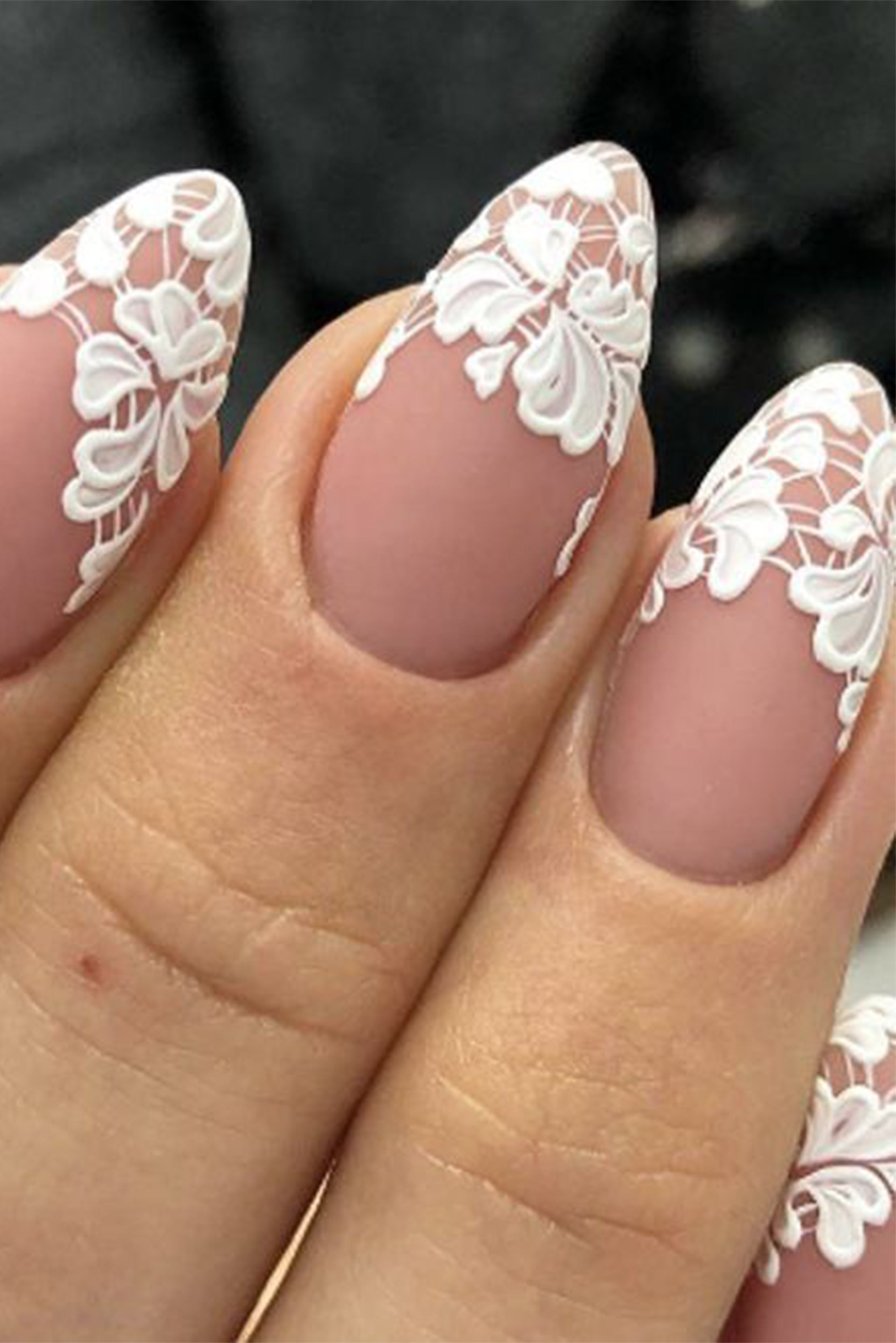 Gros plan sur des ongles style french manucure mais à la place de la partie blanche au bout des ongles il y a un dessin style dentelle