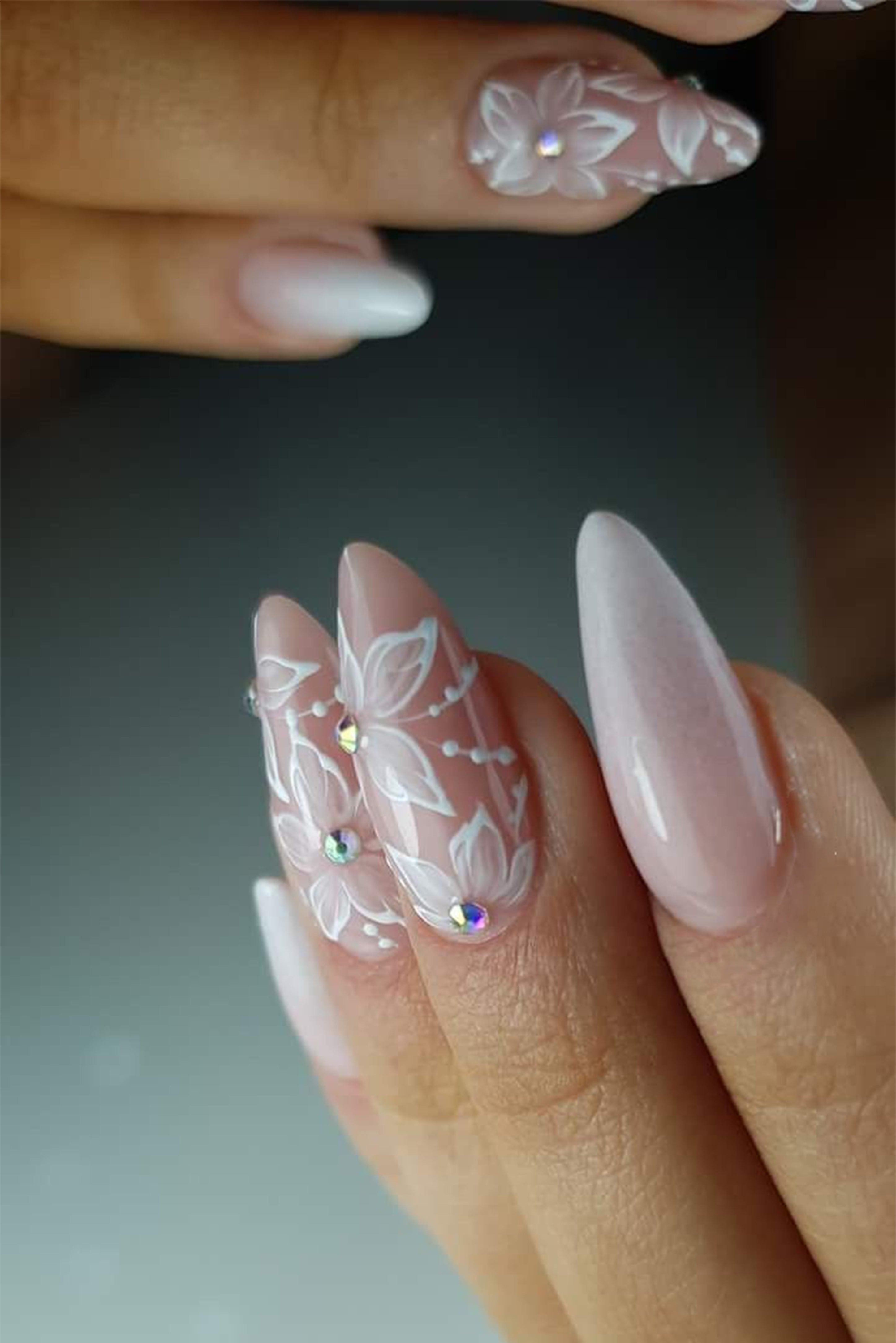 Ongles de mariées long en forme d'amande avec une manucure nude et des dessins style dentelle et des cristaux sur deux doigts