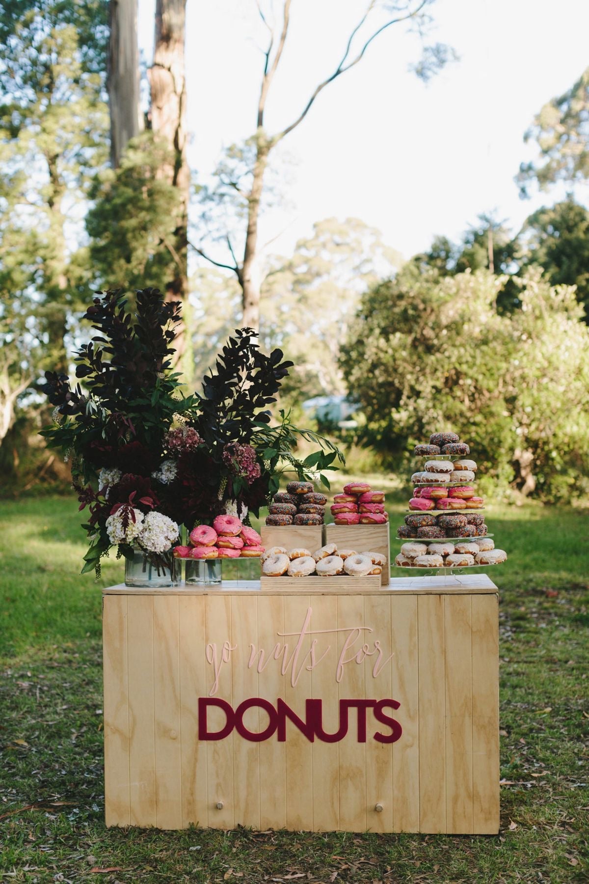 table en bois avec des donuts rose, violette et beige pour un animation mariage dans un jardin