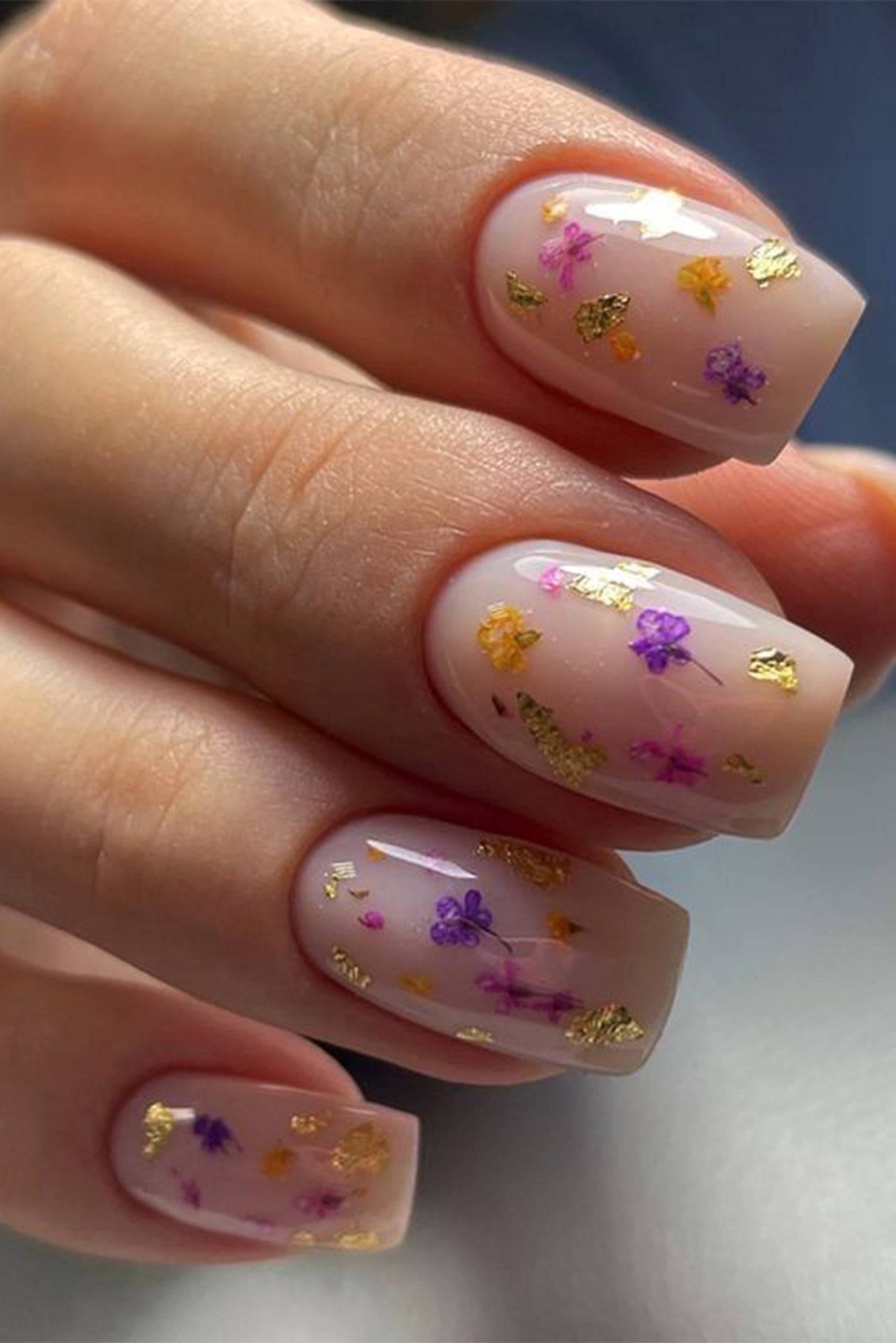 Ongles pour mariées avec une forme carrée et une couleur nude et une touche de fleurs et papier d'or incrustés