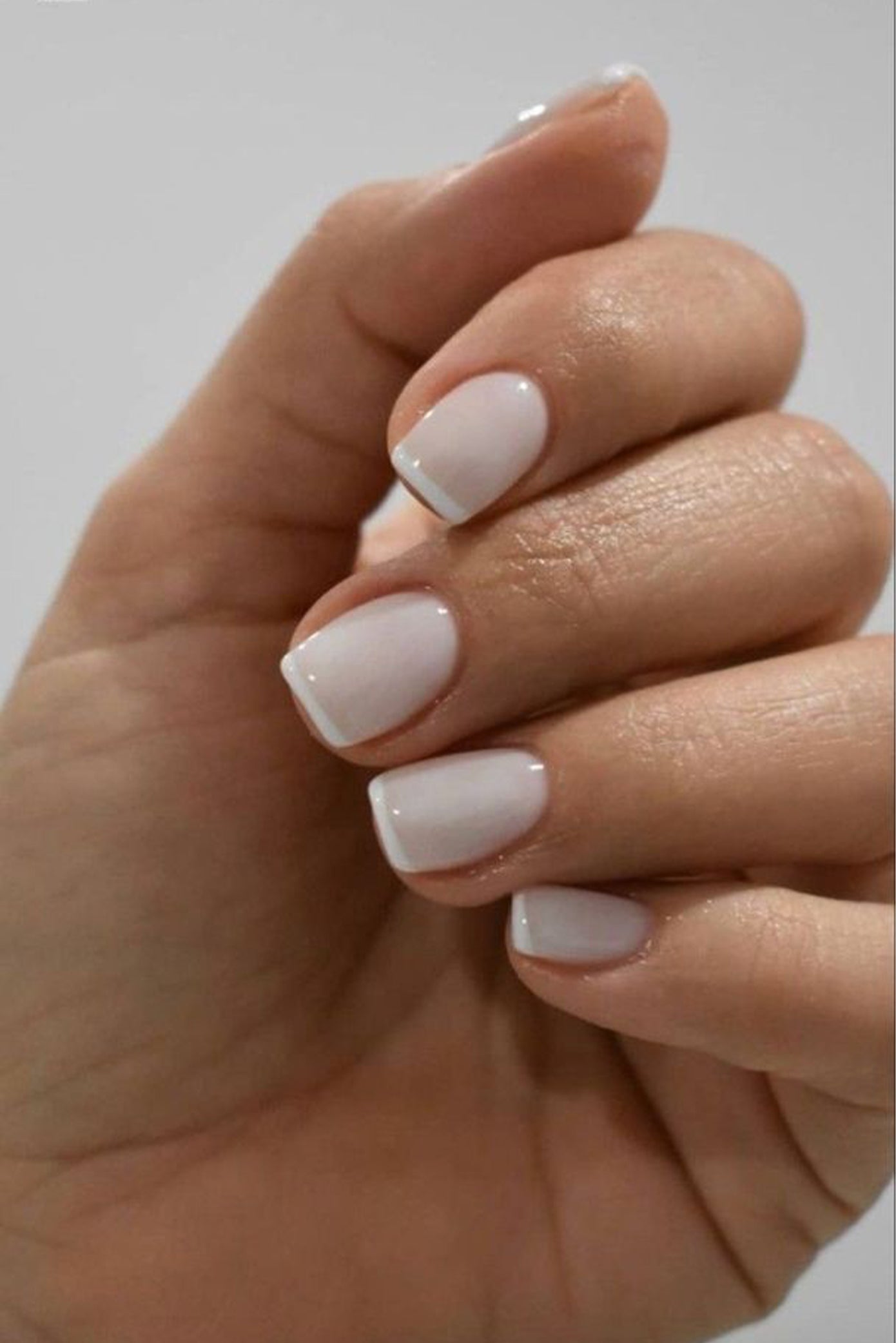 Gros plan d'une main de mariée avec ongles courts et un vernis style french manucure