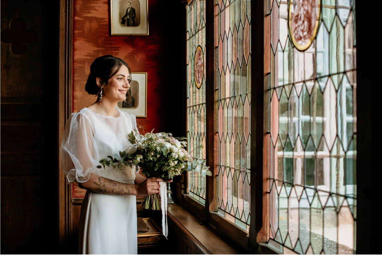 Jeune mariée souriante à coté d'une vitre  portant son ensemble de mariage et accessoires en perles