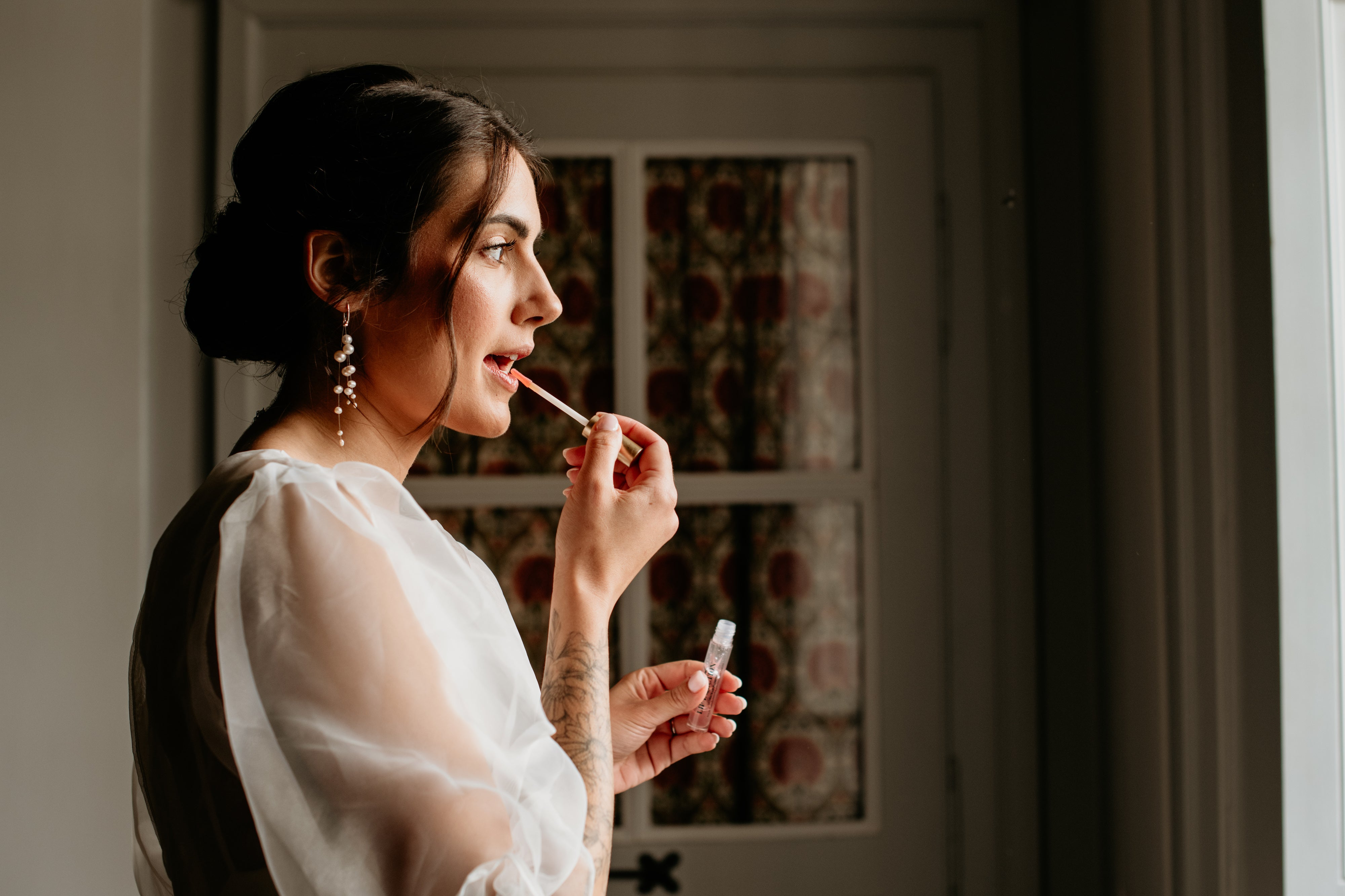 Jeune femme se mettant du gloss de profil montrant ces boucles d'oreilles de mariage asymétrique en perles naturelles