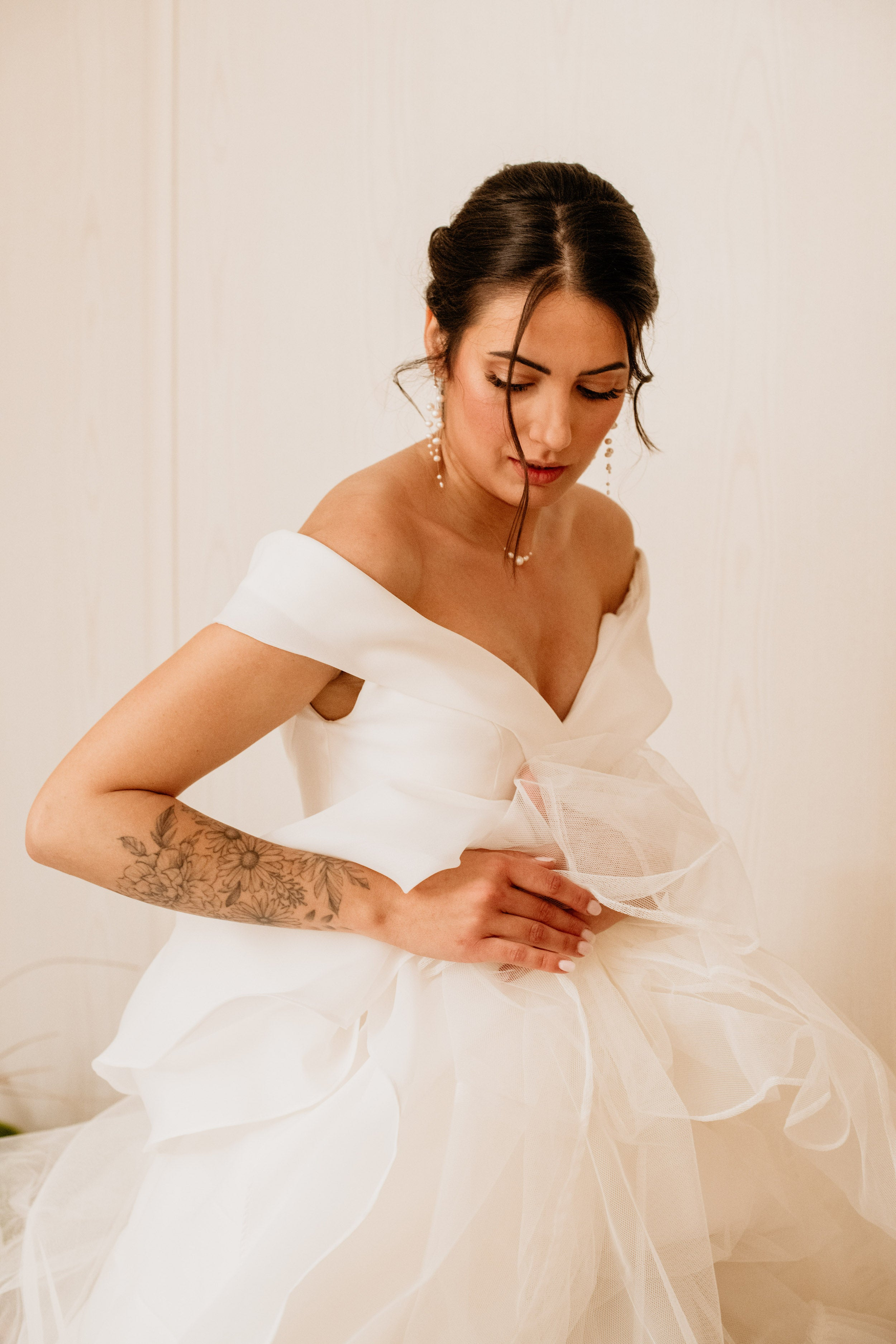 Femme de profil touchant sa robe de mariée montrant ces bijoux en perles naturelles grâce à a sa coiffure de mariage