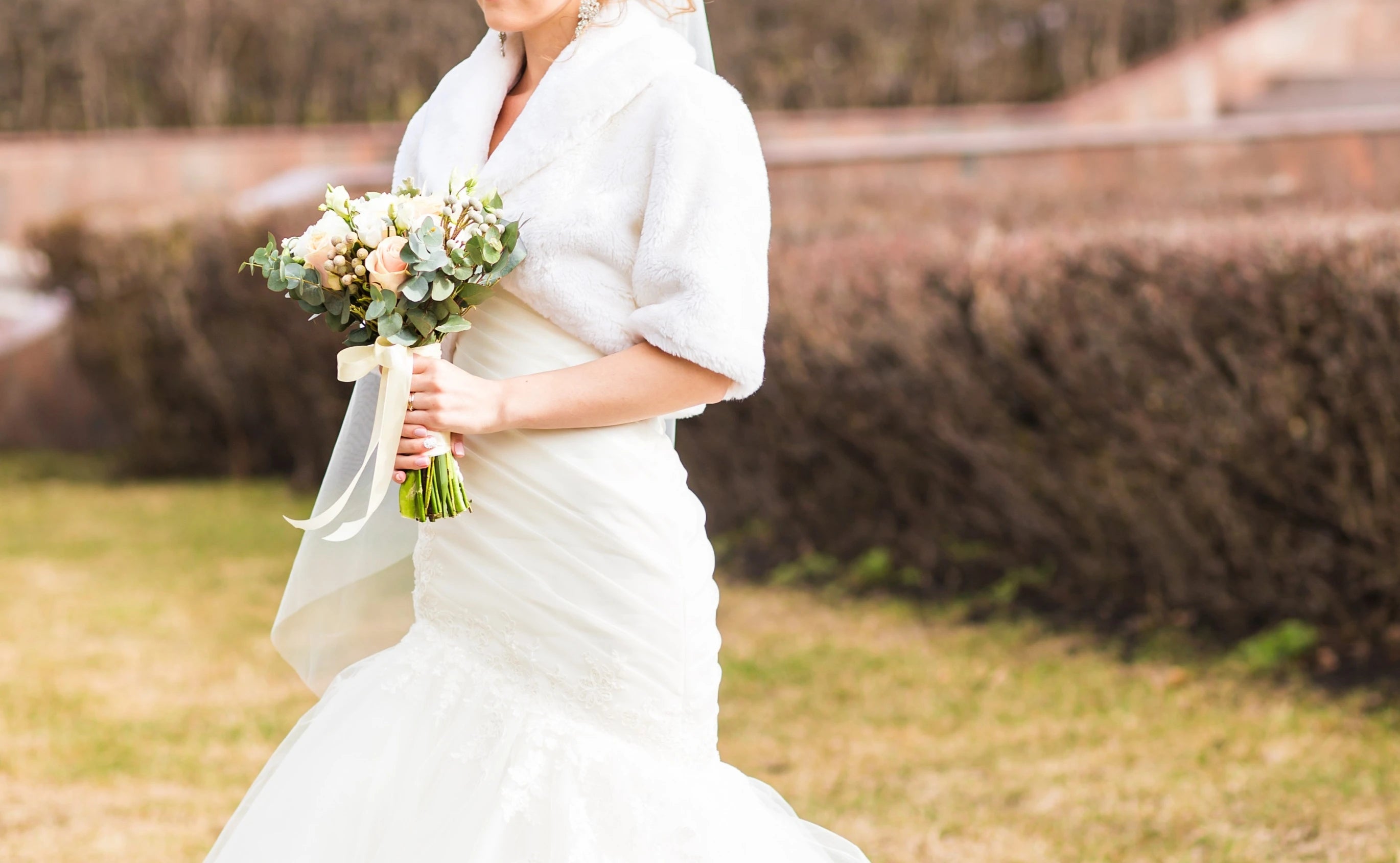 Buste d'une mariée d'hiver portant sa robe ajustée avec son châle de mariage et avec une bouquet de fleurs dans les mains