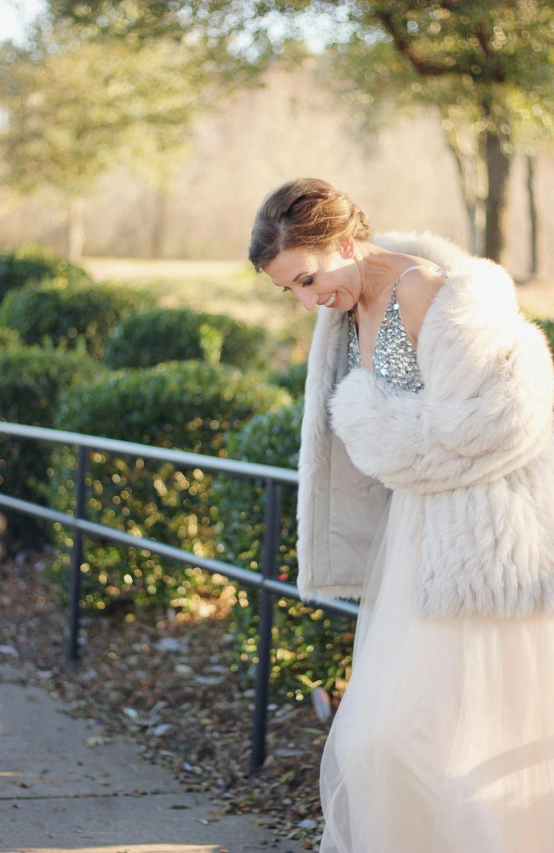 Mariée d'hiver souriante portant au dessus de sa robe de mariage une veste en fausse fourrure 