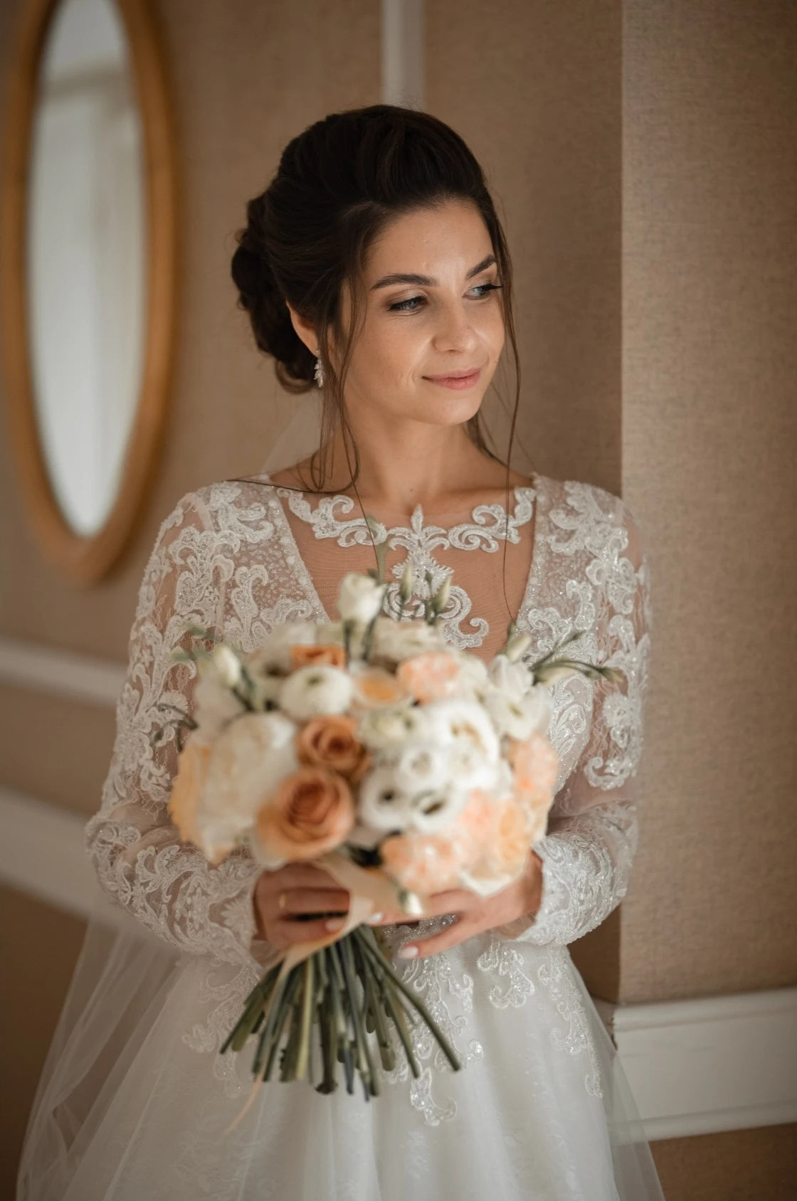 Mariée avec une robe en dentelle à manches longues avec un bouquet de fleurs à la main