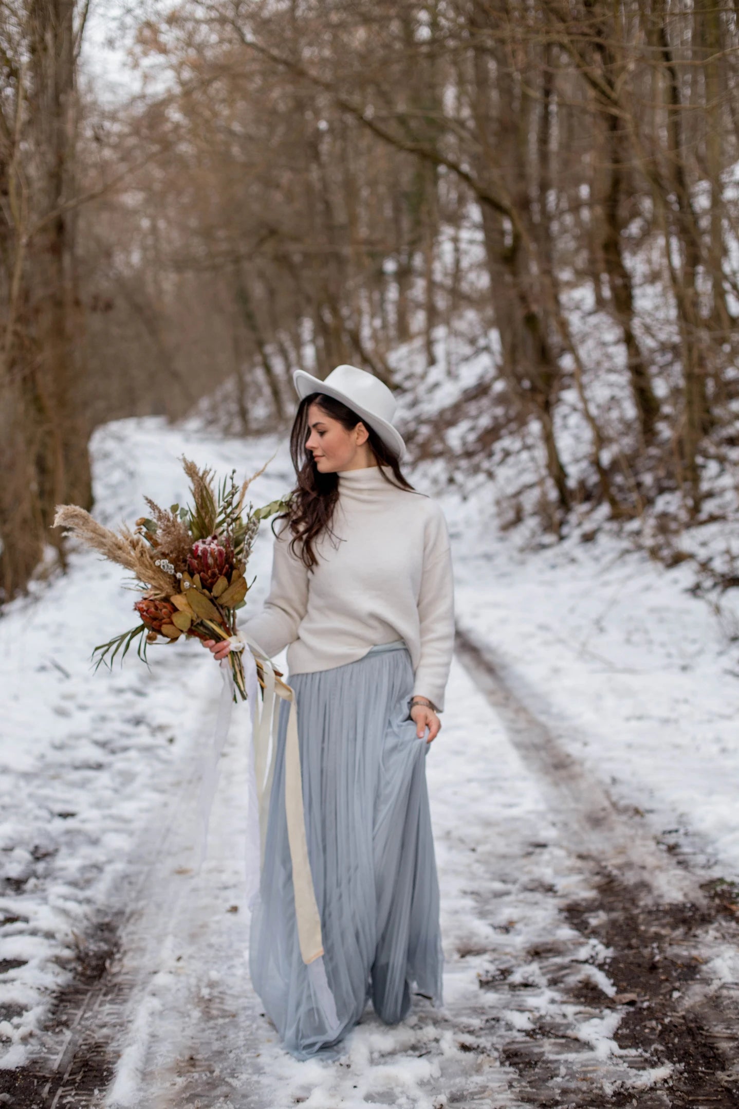 Femme marchant dans un chemin enneigé avec un bouquet de fleurs séchées à la main