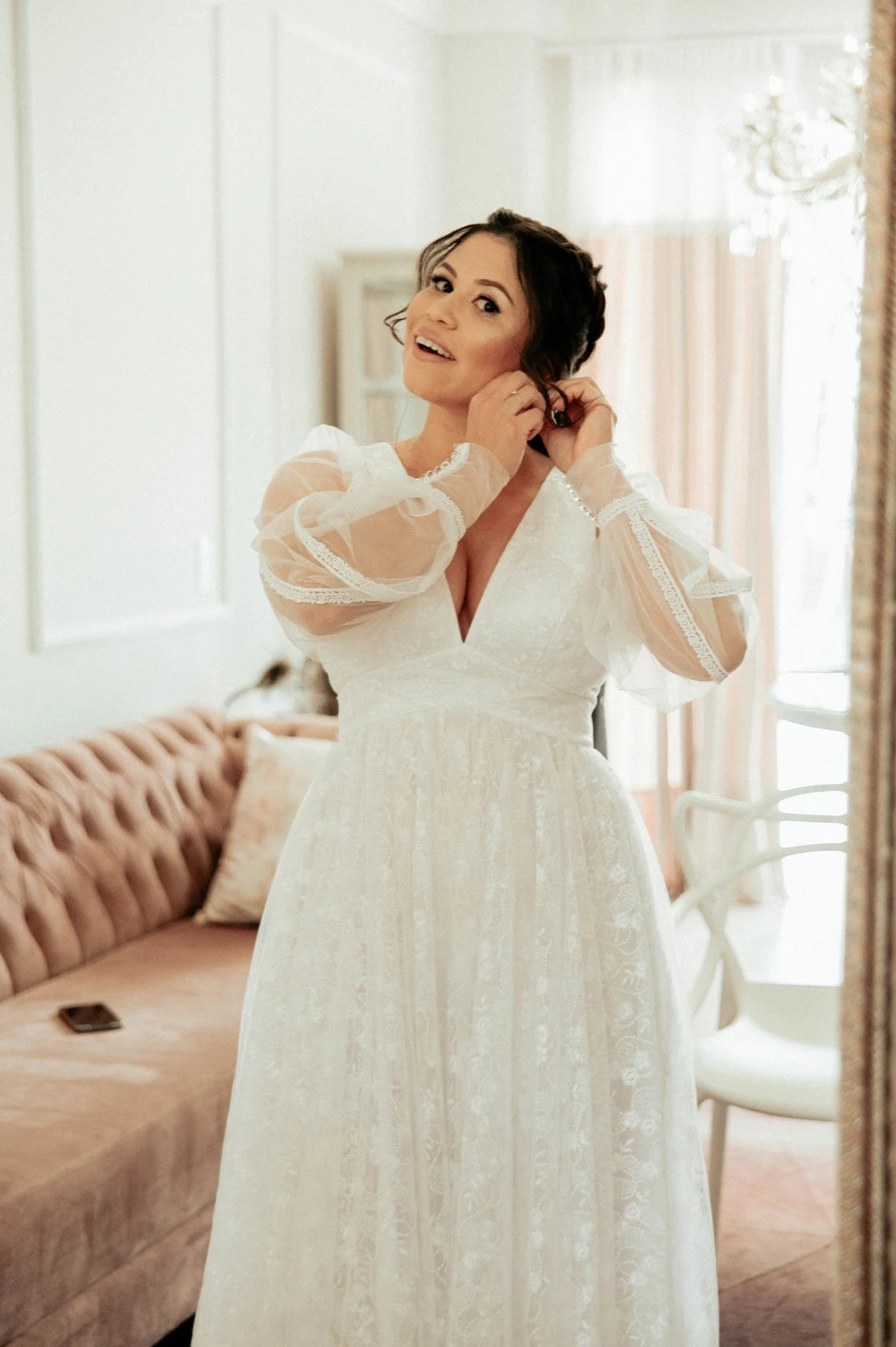 Mariée avec une robe avec des manches longues bouffante qui mets ses boucles d'oreilles de mariage