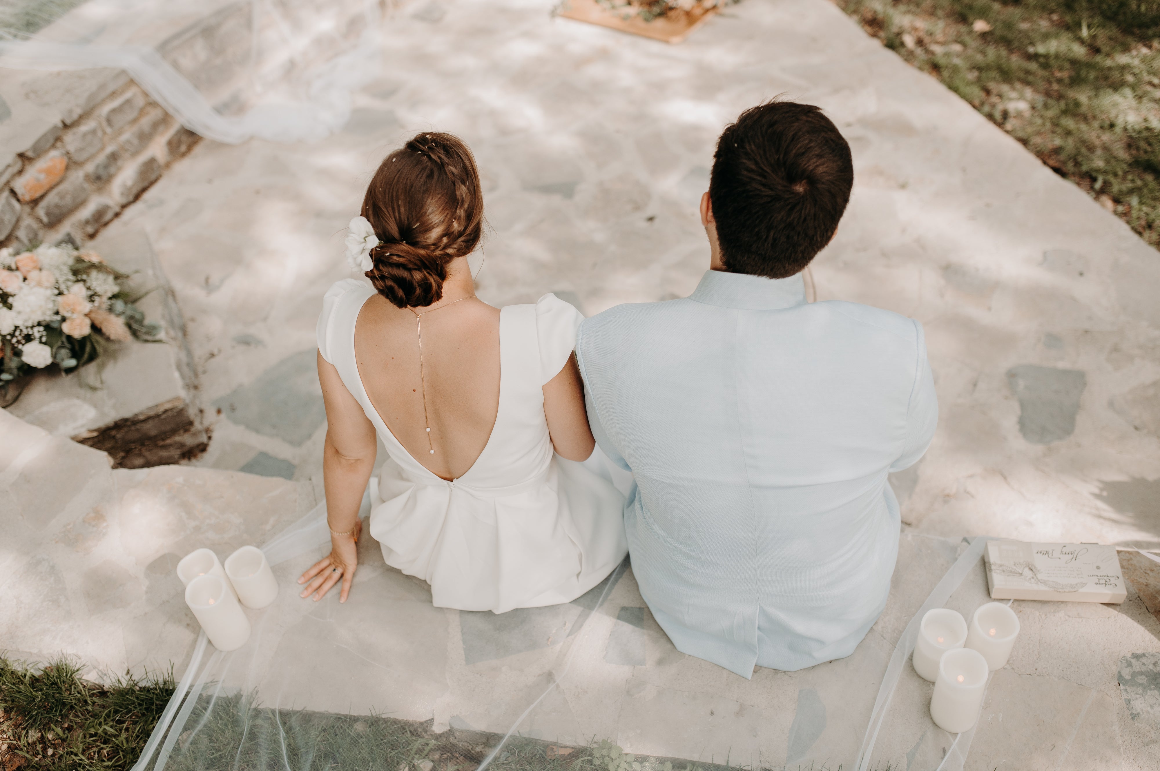 Deux mariés de dos dans leurs tenues de mariage avec la femme portant une robe à décolleté de dos plongeant  montrant son bijou de dos