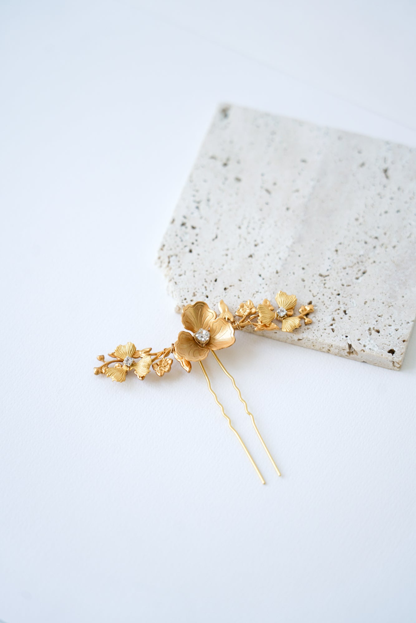 pic à cheveux de mariage doré avec un fleur et des strass posé sur une pierre beige 