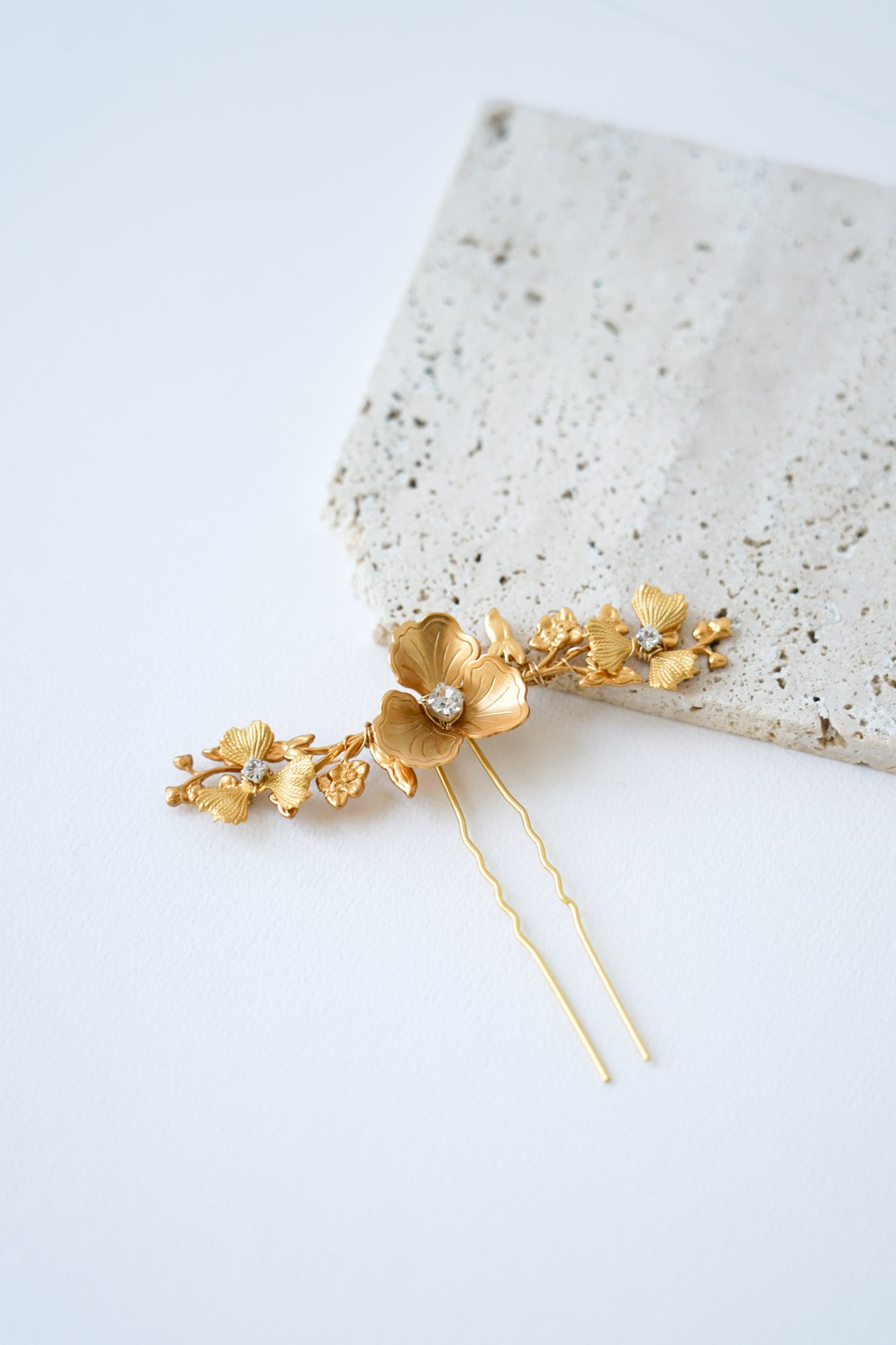 accessoire de cheveux pour mariage doré avec des fleurs, des branches et des strass sur un fond blanc