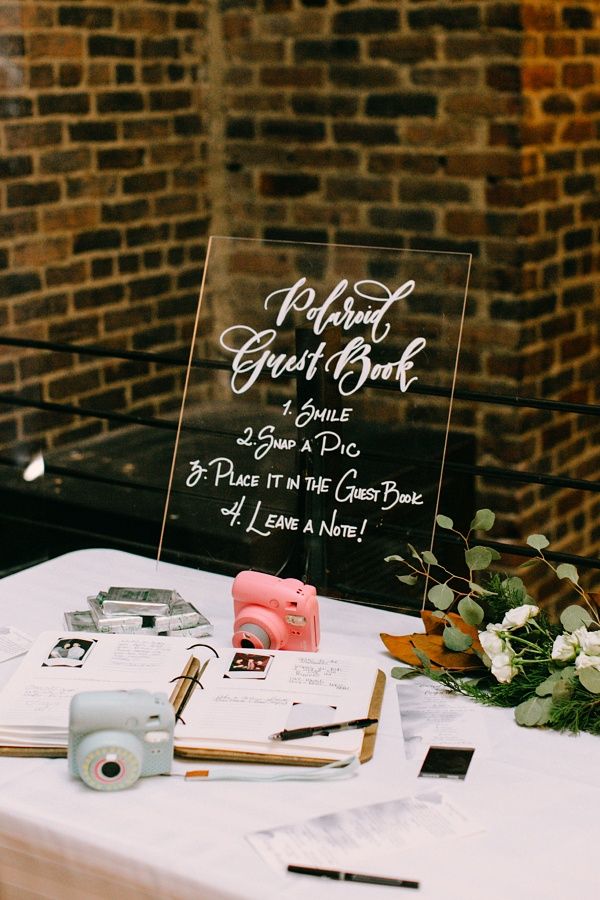 table du livre d'or d'un mariage avec deux appareils photos instantanés et un plaque transparente écrit le nom des mariés en blanc