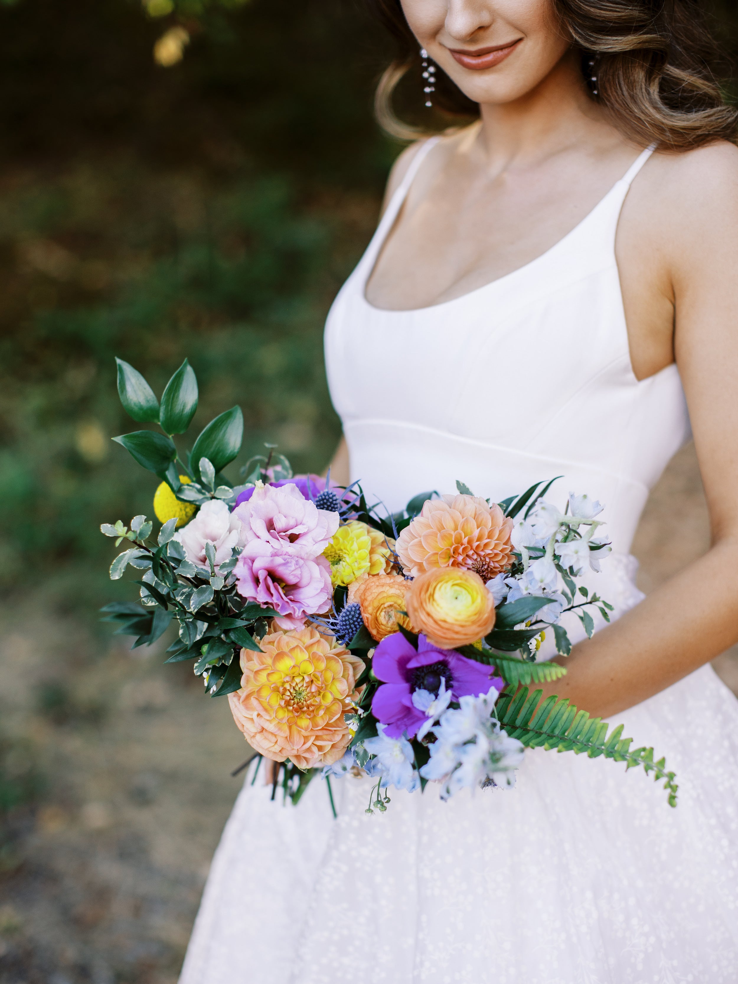 Femme tenant un bouquet pour mariée dans une robe blanche et des boucles d'oreilles en perles